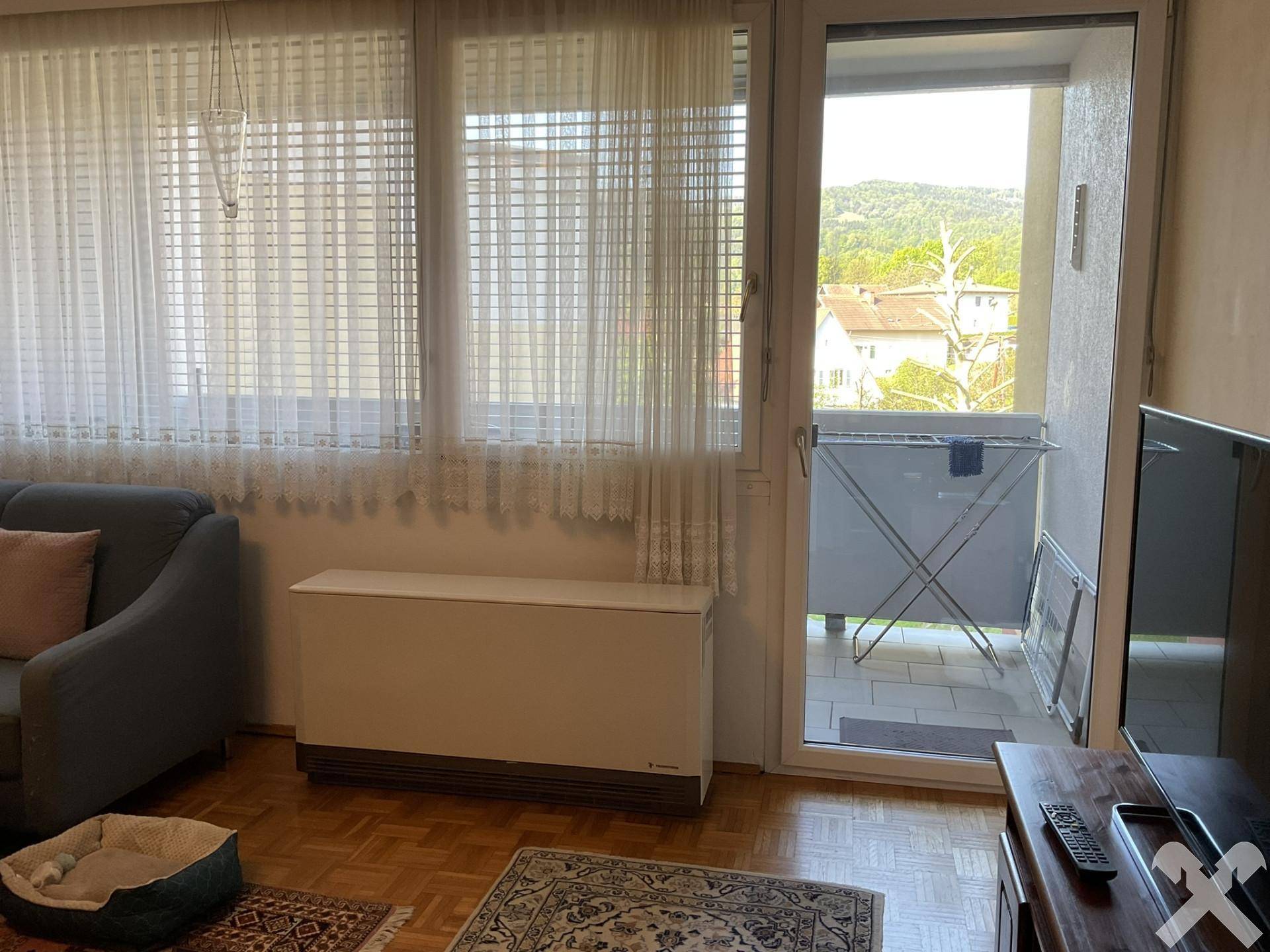 Heller Wohnbereich mit Zugang zum Balkon und Blick ins Grüne, ausgestattet mit einem Fernseher.