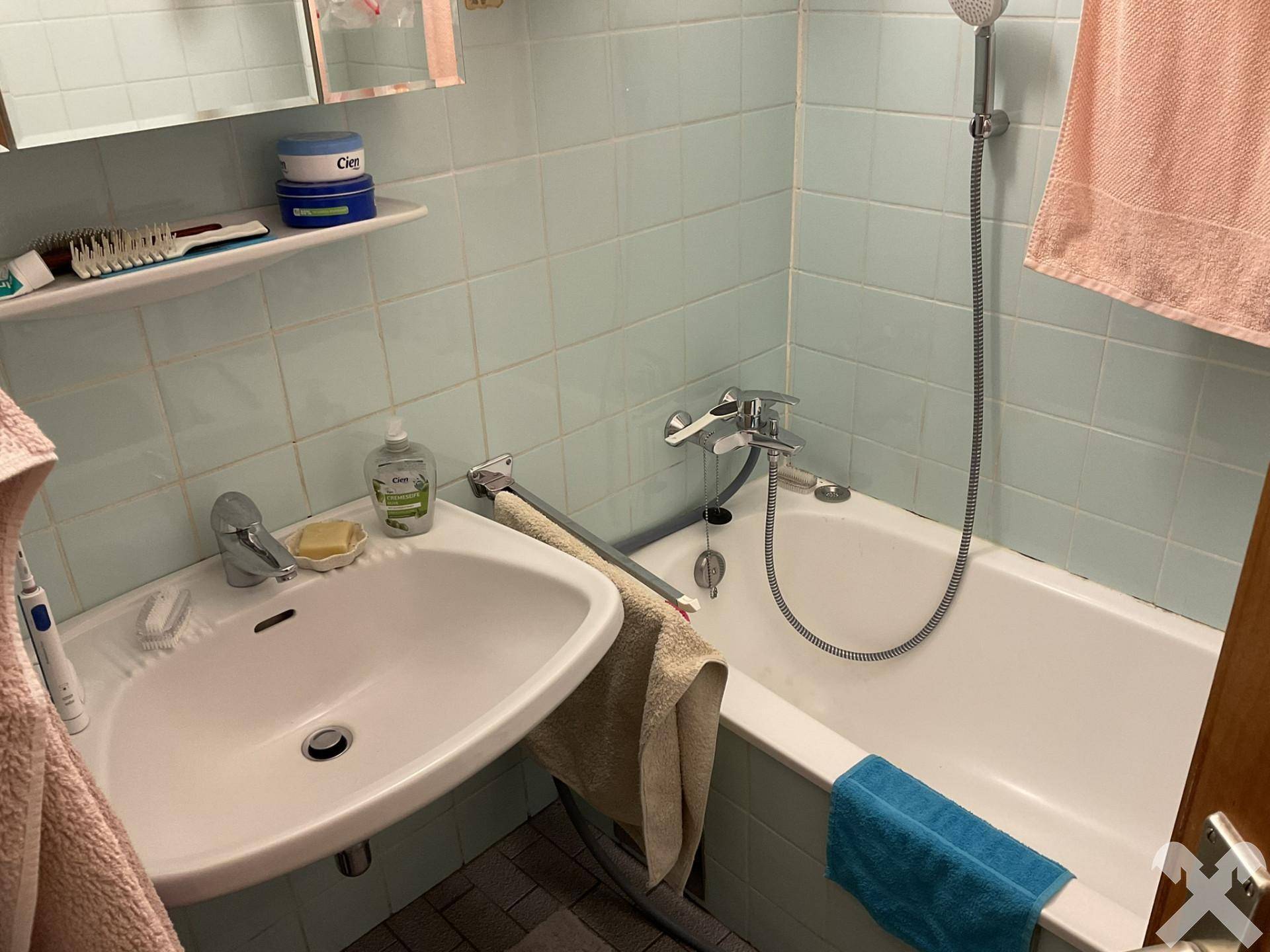 Badezimmer mit Badewanne, Waschbecken und hellblauen Fliesen, funktional und gut beleuchtet.