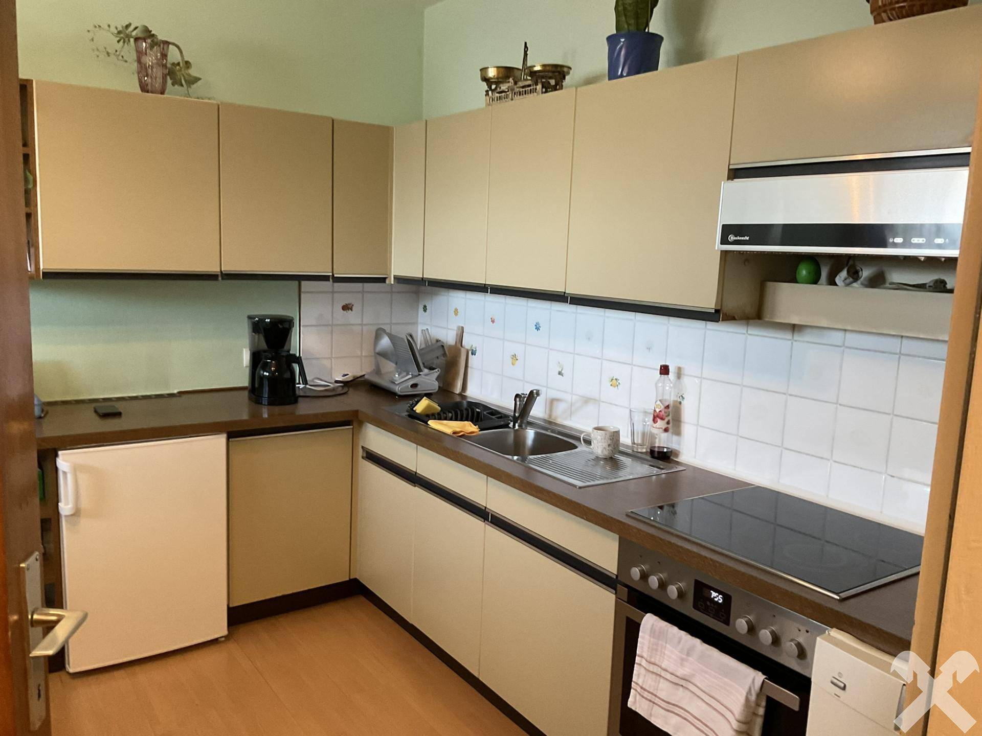 Funktionale Küche mit beigen Schränken, Fliesenrückwand und integrierten Elektrogeräten, gut ausgestattet.