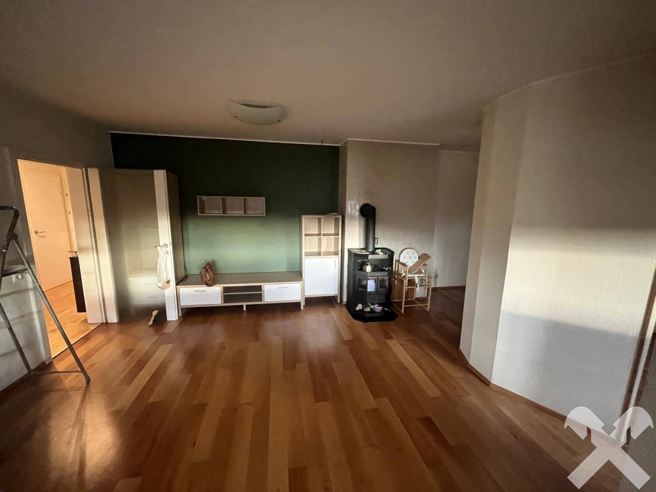 Gemütliches Wohnzimmer mit Holzofen, Parkettboden und einer dunkelgrünen Akzentwand.