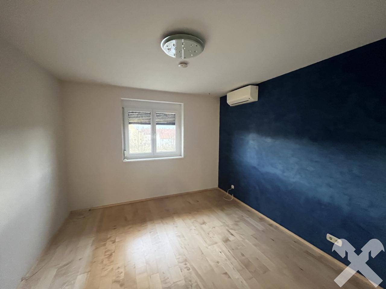 Geräumiges Schlafzimmer mit Parkettboden, blauer Akzentwand und Klimaanlage.