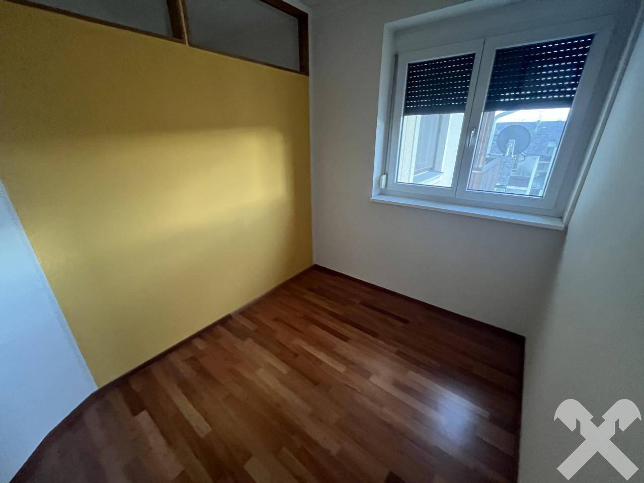Kleines Zimmer mit Parkettboden und gelber Akzentwand, ideal als Büro oder Gästezimmer.