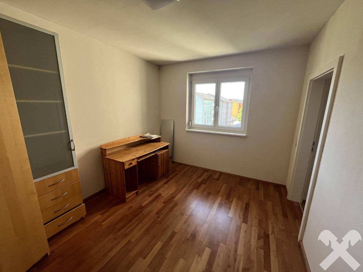 Helles Schlafzimmer mit Parkettboden, Fenster und einfacher Möblierung.