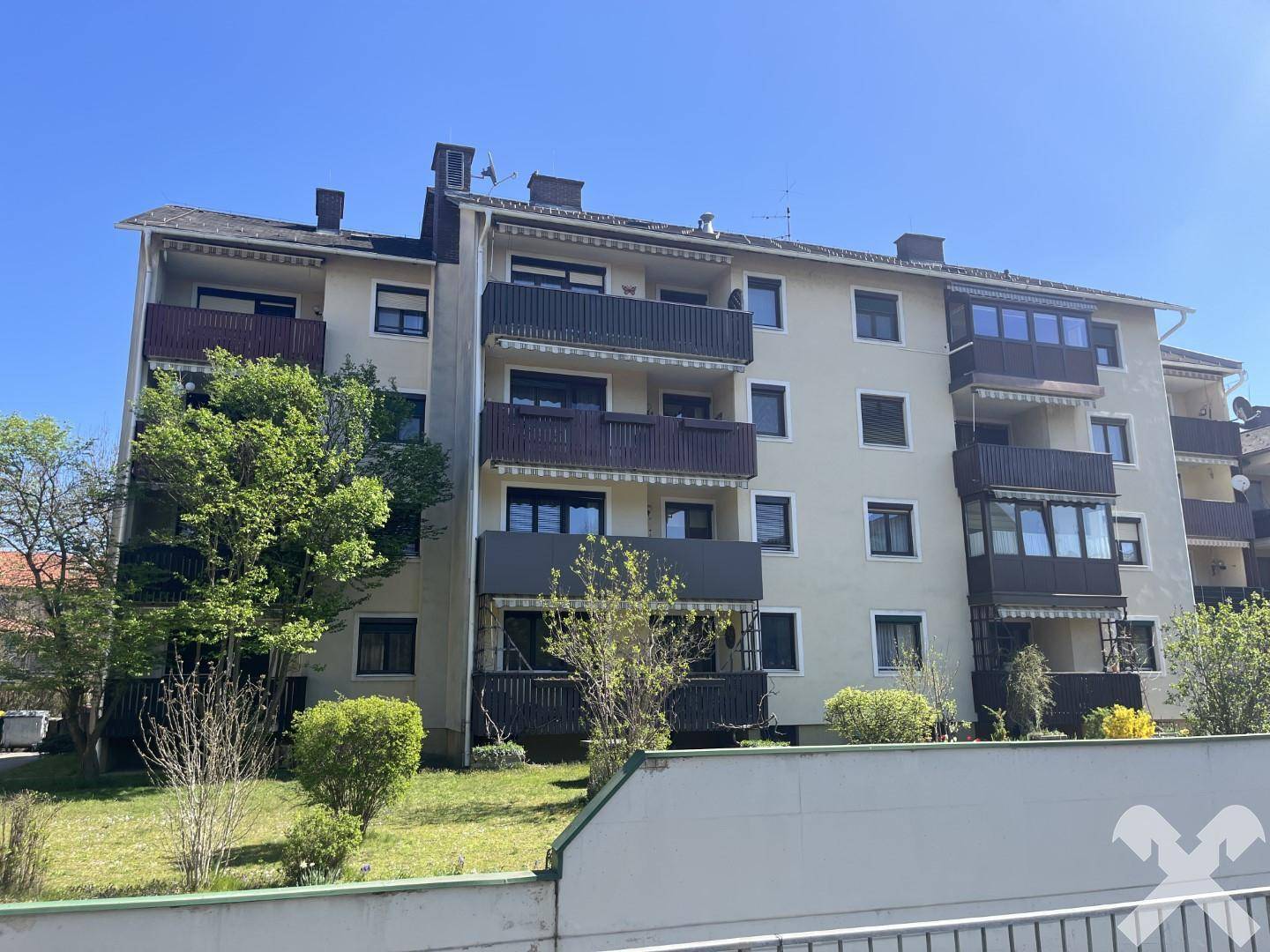 Ansicht eines Mehrfamilienhauses mit mehreren Balkonen und umliegender Bepflanzung.