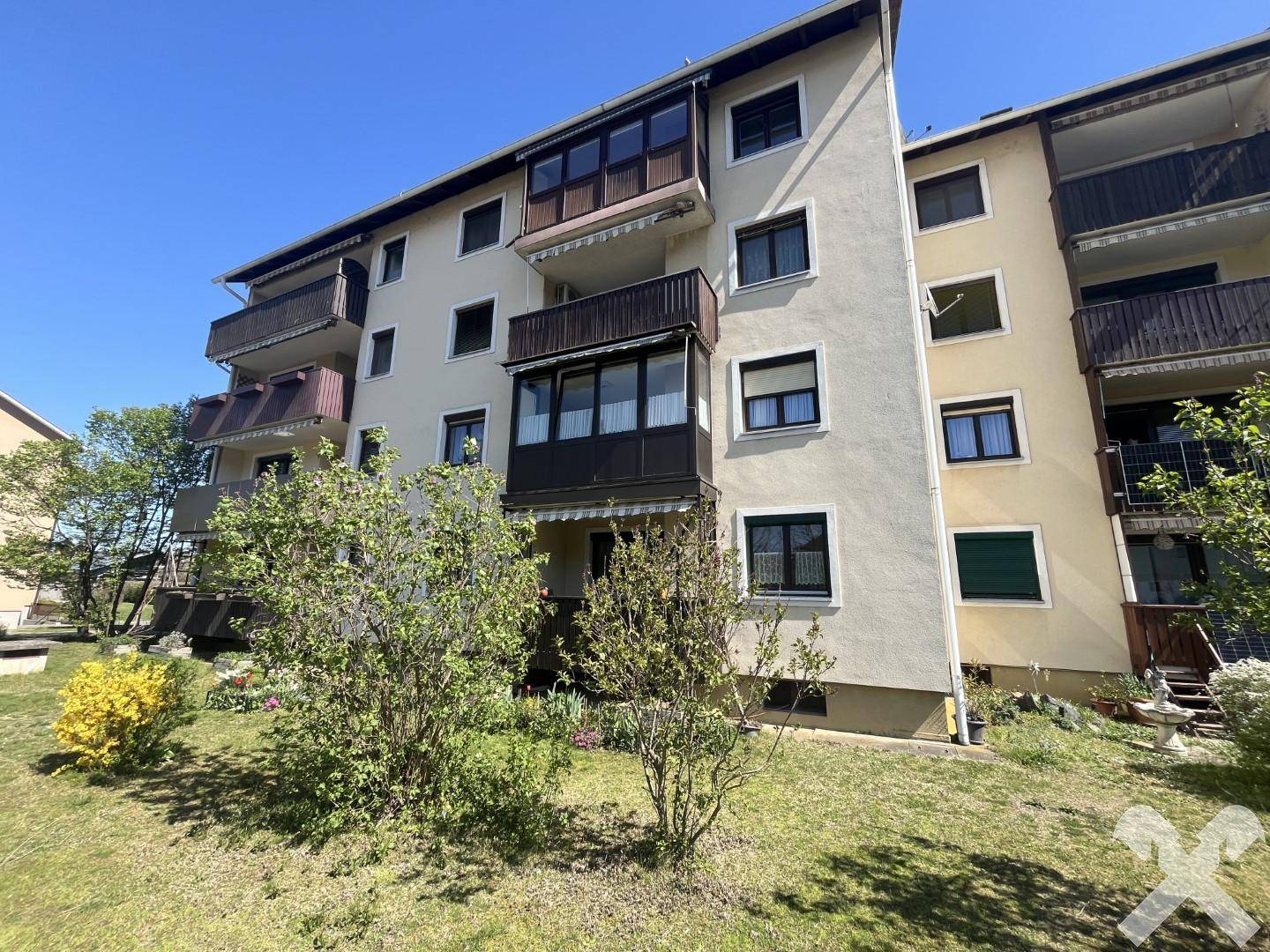 Mehrfamilienhaus mit Balkonen und gepflegter Grünfläche an einem sonnigen Tag.