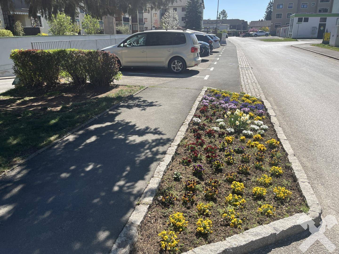 Außenbereich mit Parkplätzen und farbenfrohen Blumenbeeten entlang der Straße.