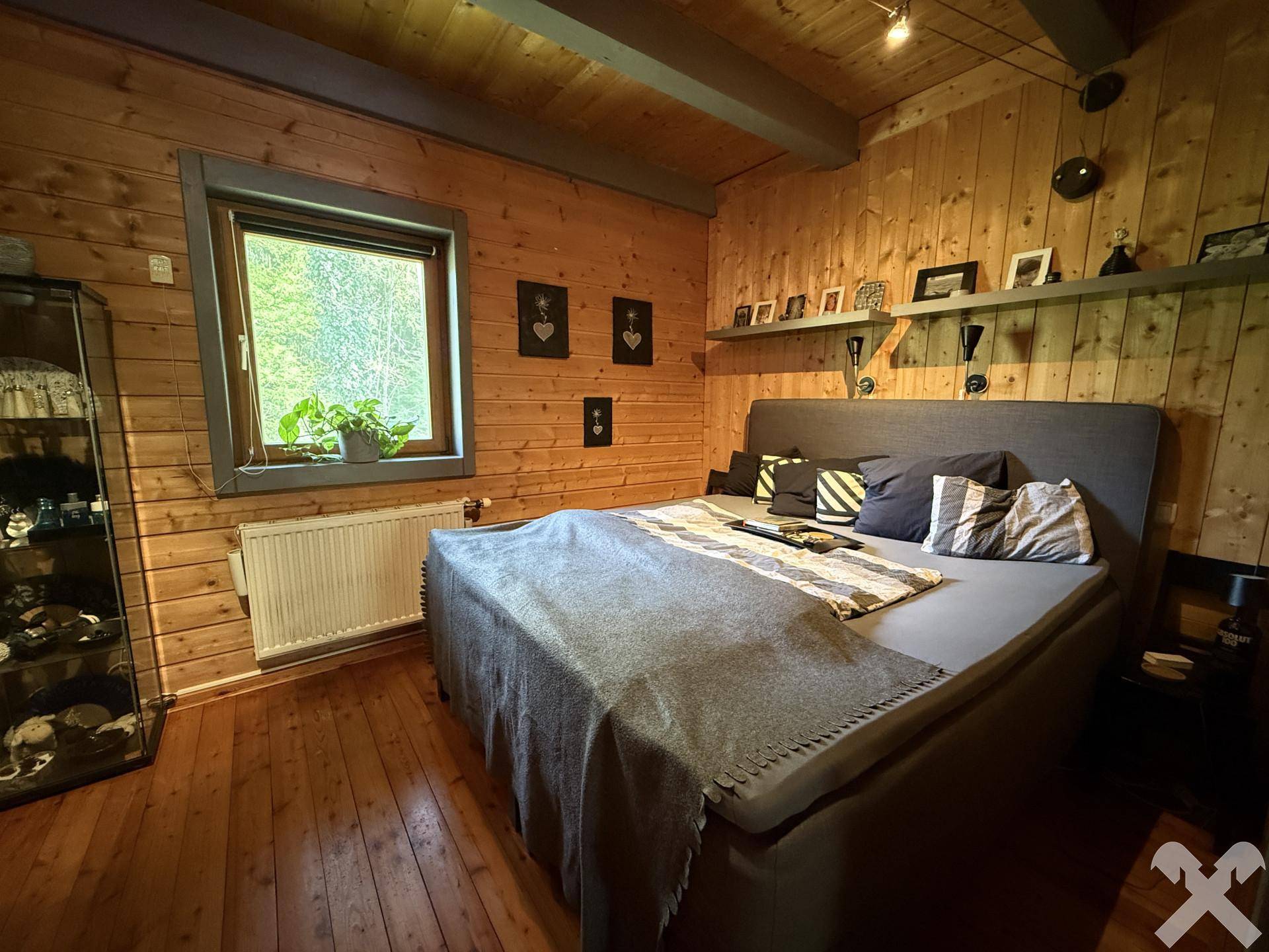 Gemütliches Schlafzimmer mit Holzwänden, Holzboden und Fenster mit Blick ins Grüne.