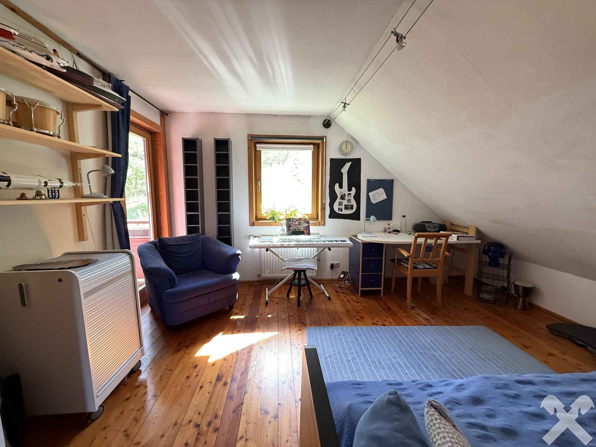 Helles Schlafzimmer im Dachgeschoss mit Holzboden, Schreibtisch und Blick ins Grüne.