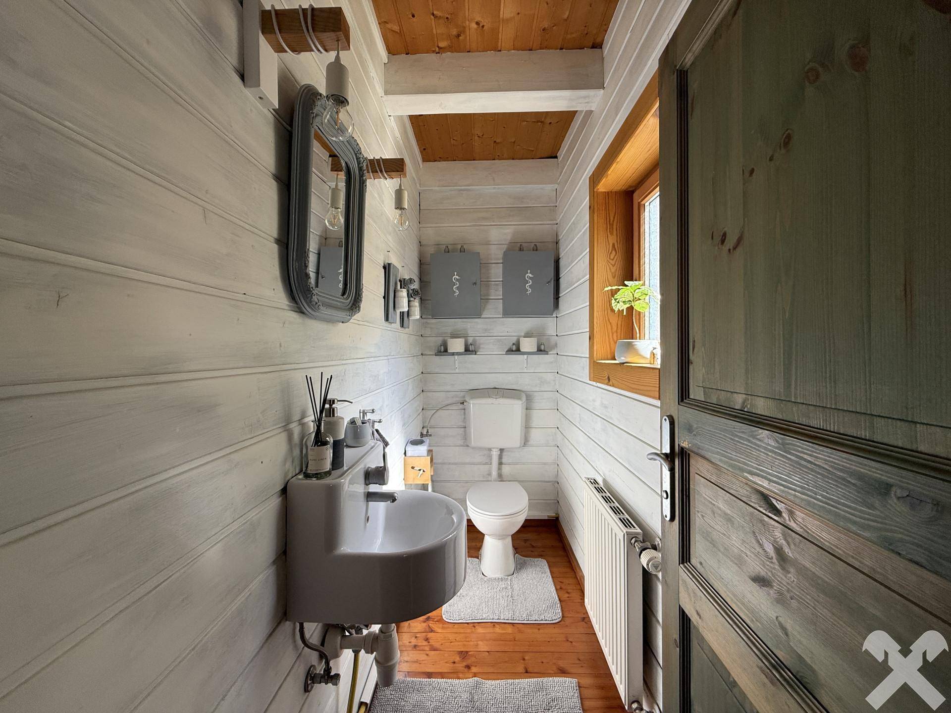 Kleines Gäste-WC mit weiß gestrichenen Holzwänden, Fenster und Holzboden.
