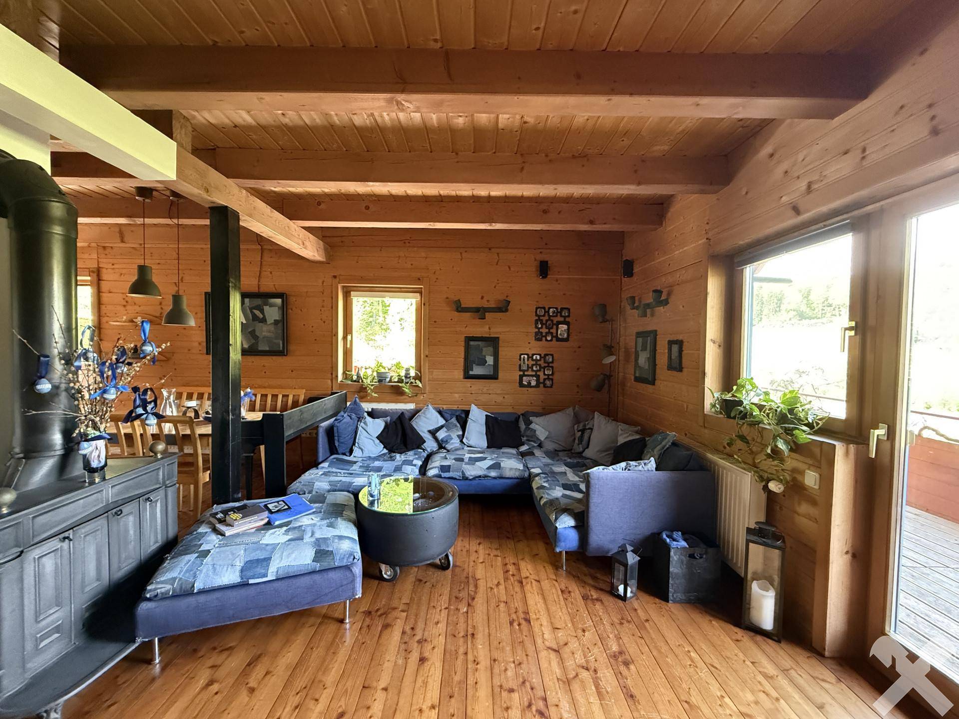 Geräumiges Wohnzimmer mit Holzwänden, Holzbalkendecke und Zugang zur Terrasse.