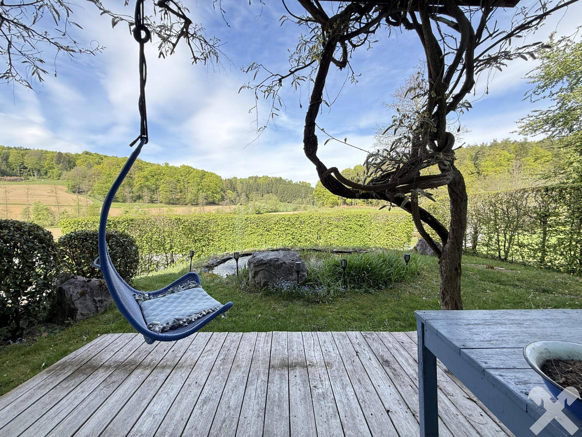 Gepflegter Garten mit Holzterrasse, Teich und Schaukel in ländlicher Umgebung.