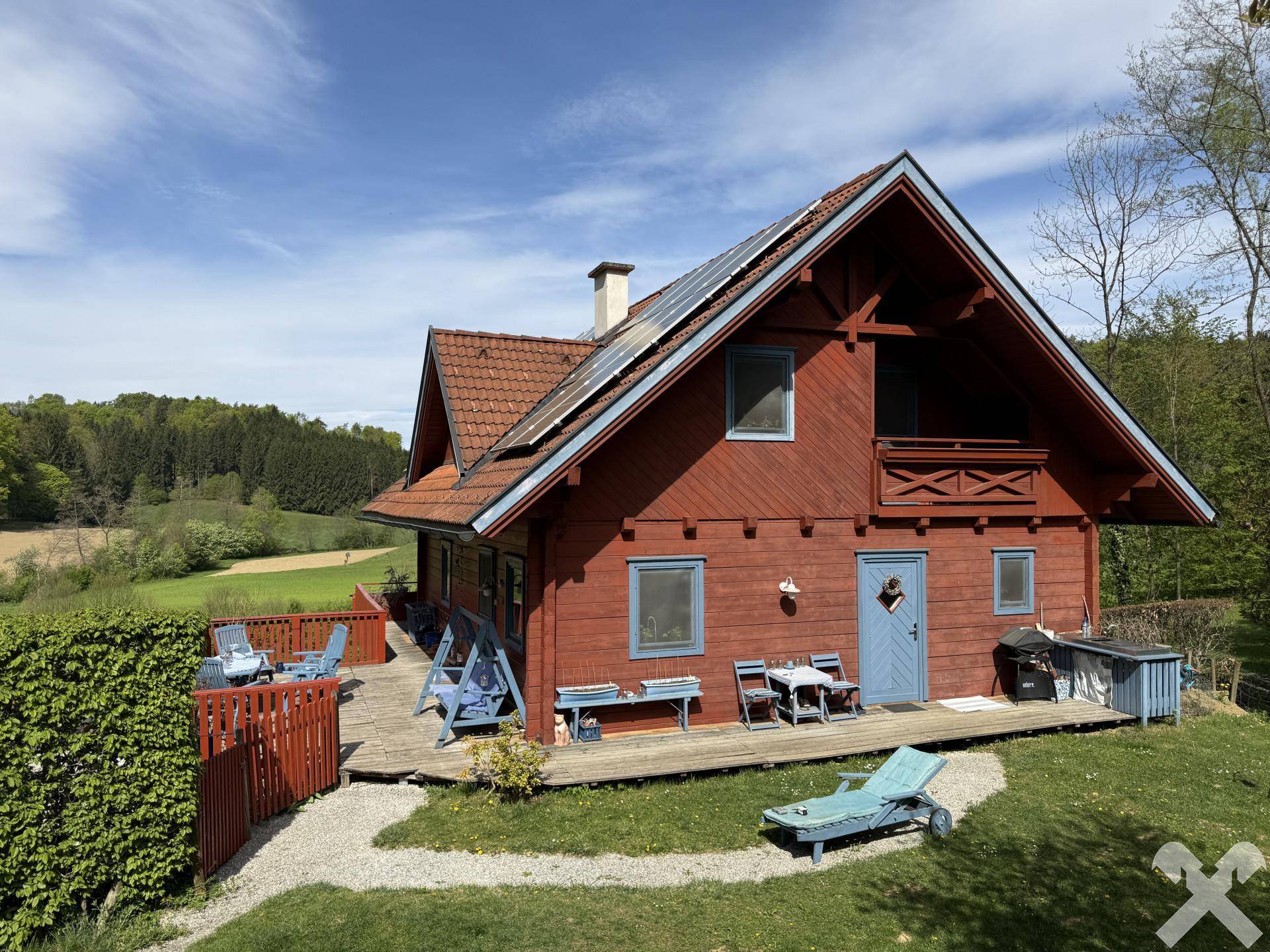 Hausfassade mit großer Holzterrasse und weitläufigem Garten in sonniger Lage.