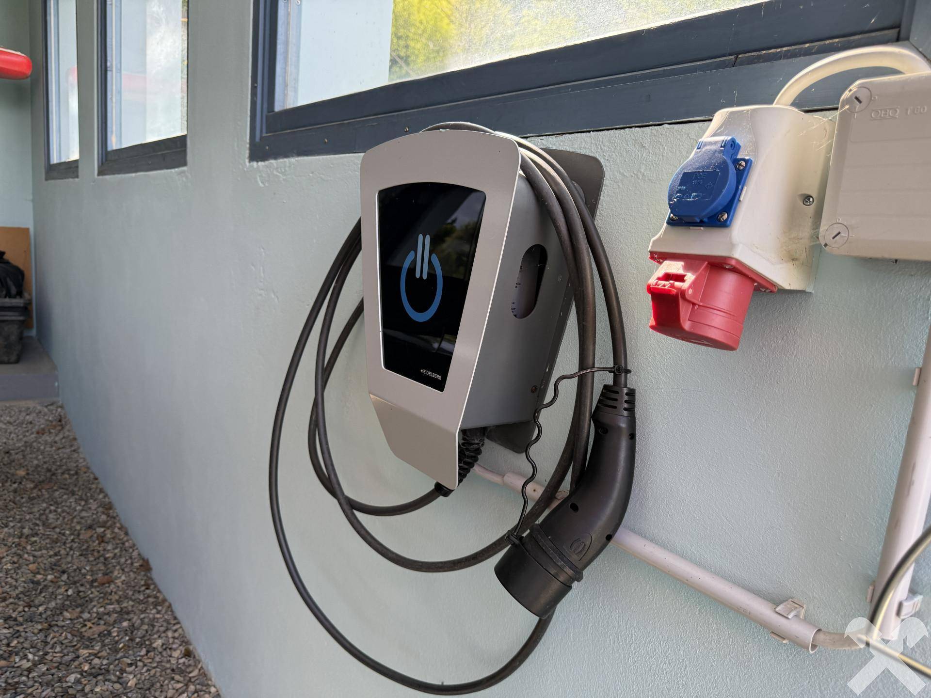 Ladestation für Elektrofahrzeuge an der Hauswand mit blauer Steckdose.