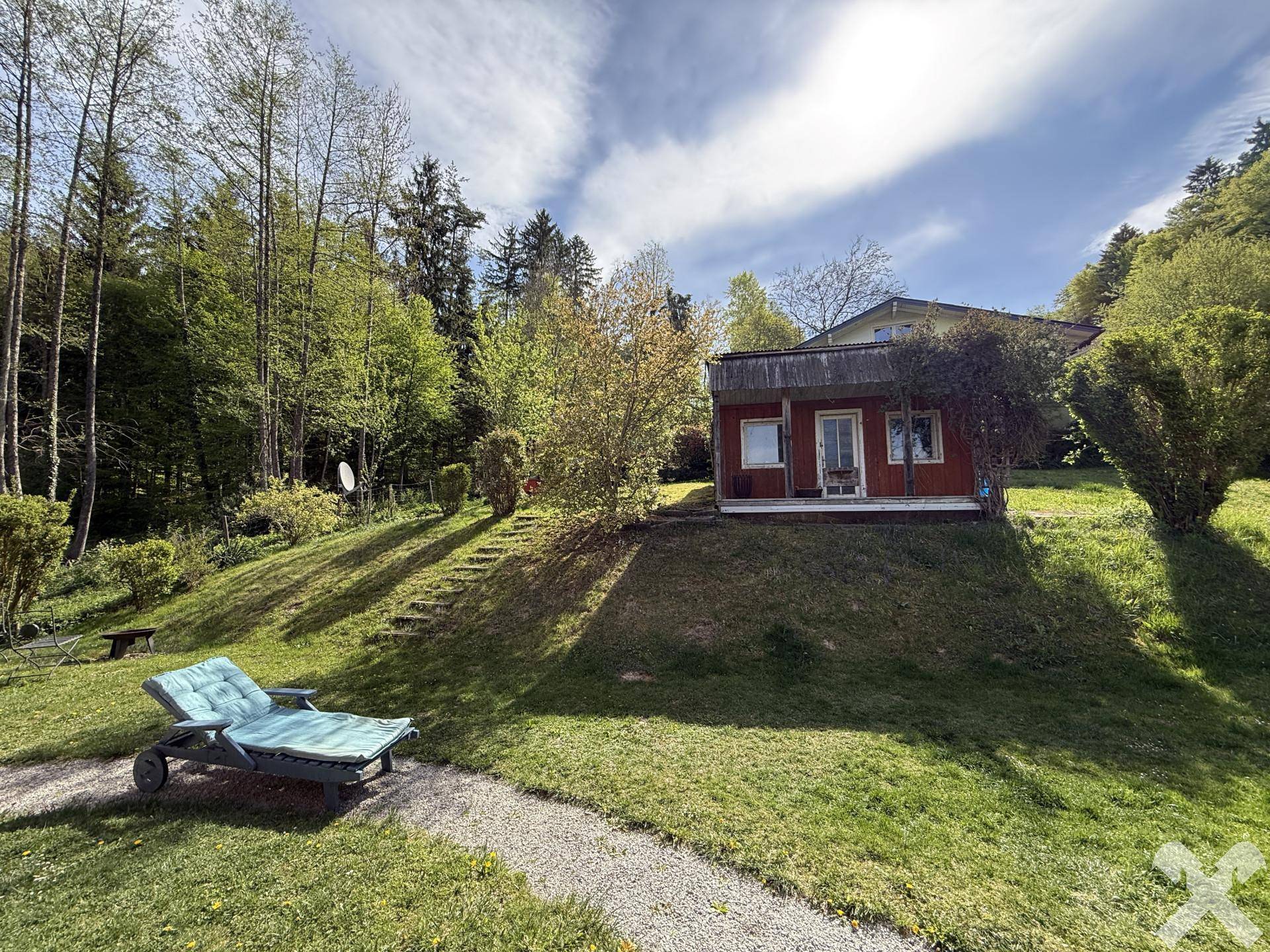 Sonniger Gartenbereich mit Liegestuhl und Blick auf die bewaldete Umgebung.