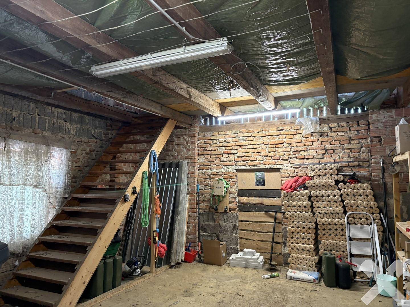 Unausgebauter Kellerraum mit Ziegelwänden, Holztreppe und Lagerbereichen.