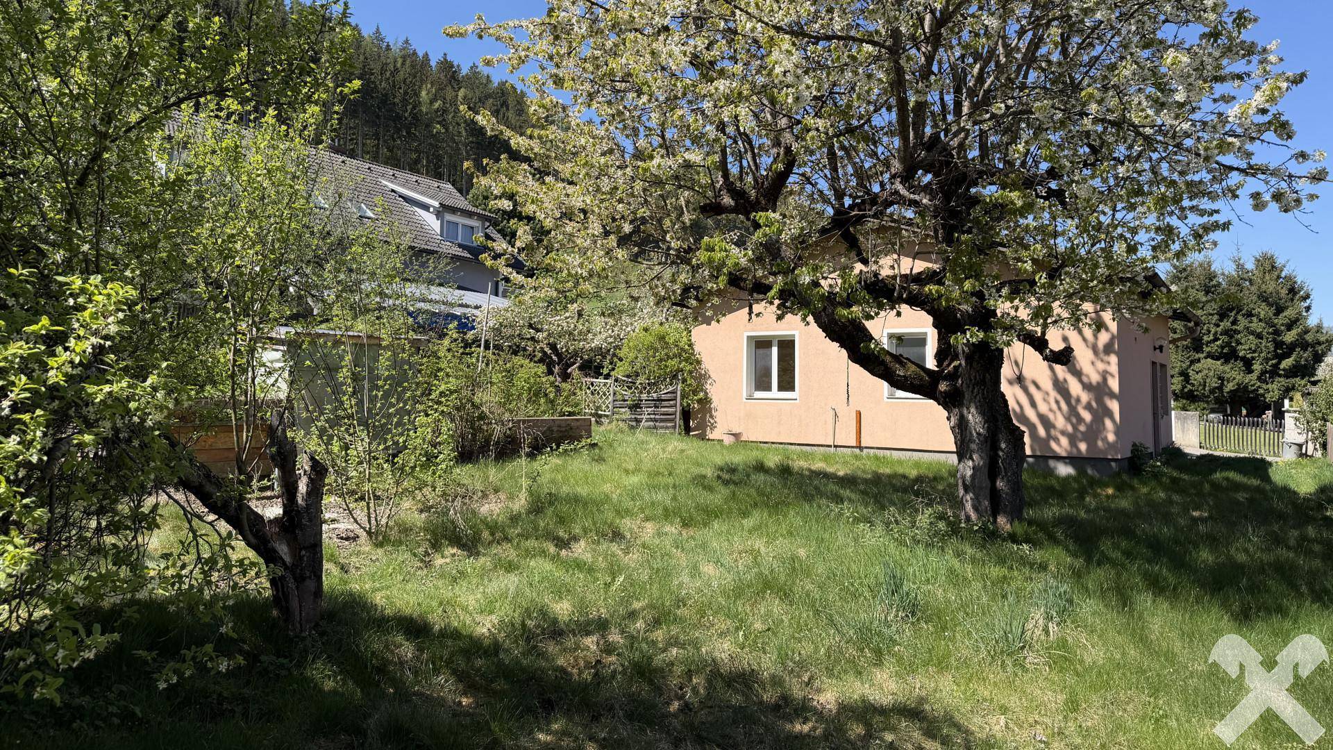 Rückansicht des Hauses mit weitläufigem Garten und blühenden Bäumen in ländlicher Umgebung.