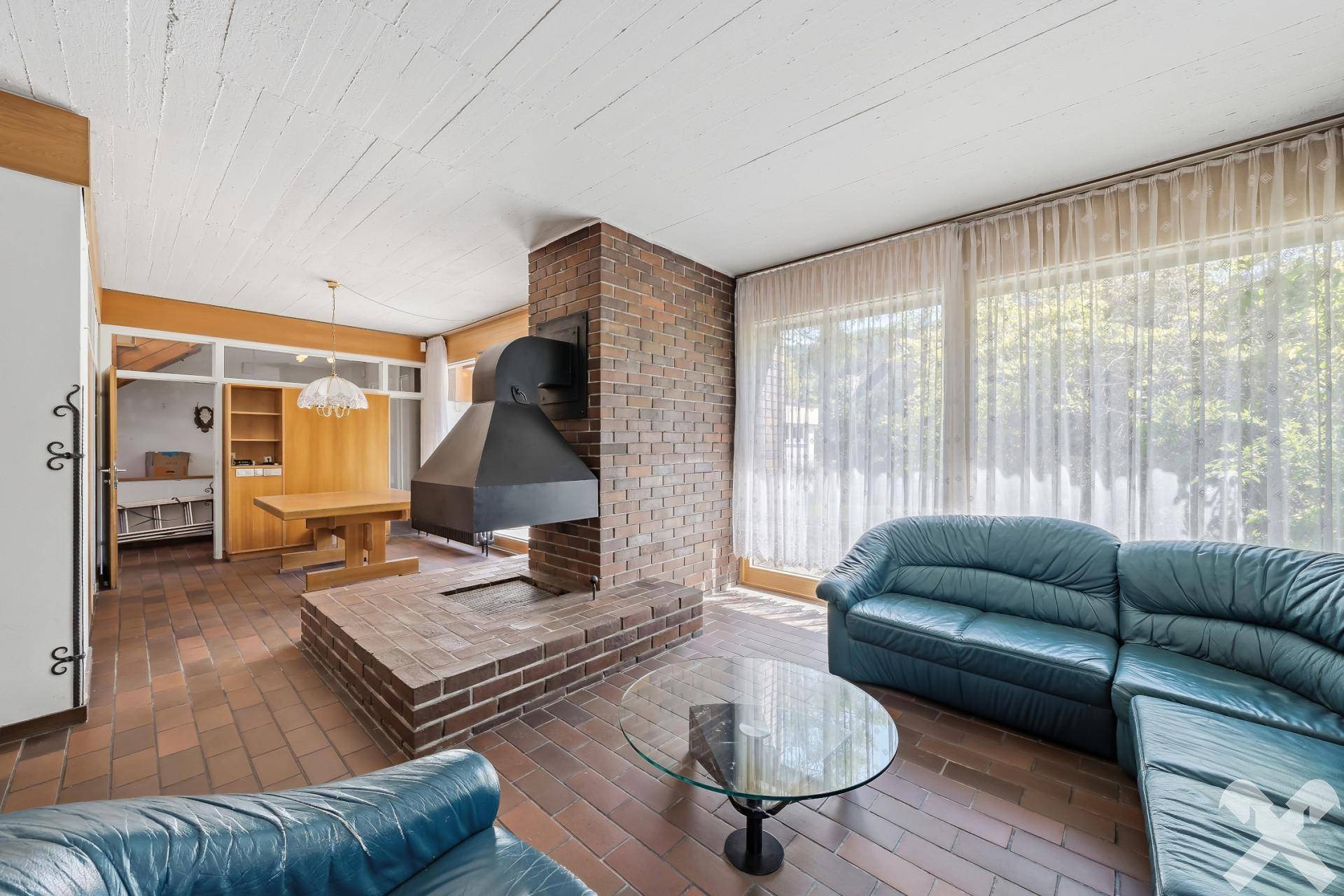 Gemütliches Wohnzimmer mit Kamin, Ledersofas und Zugang zum Gartenbereich.