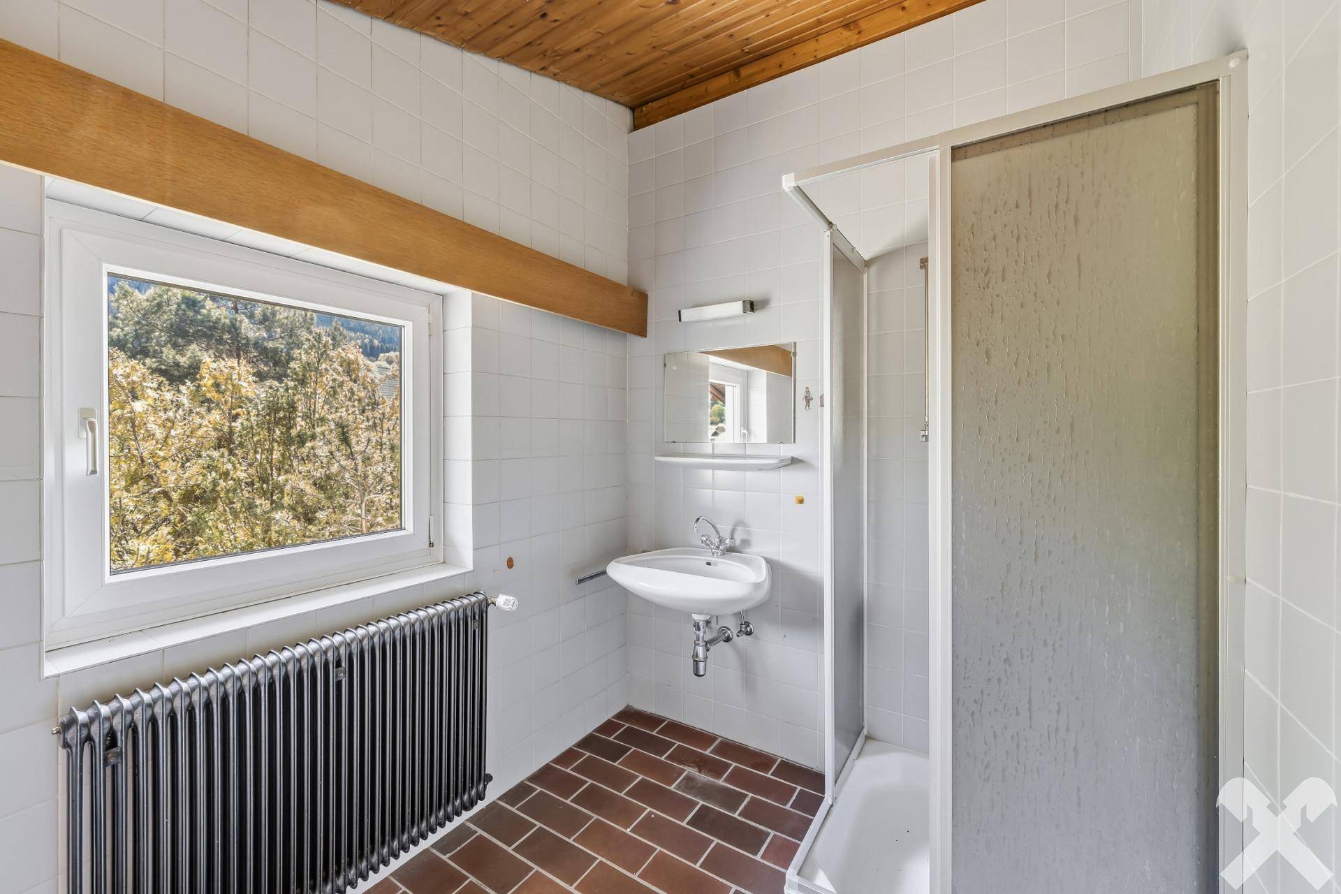 Helles Badezimmer mit Dusche, Waschbecken und Fenster mit Blick ins Grüne.