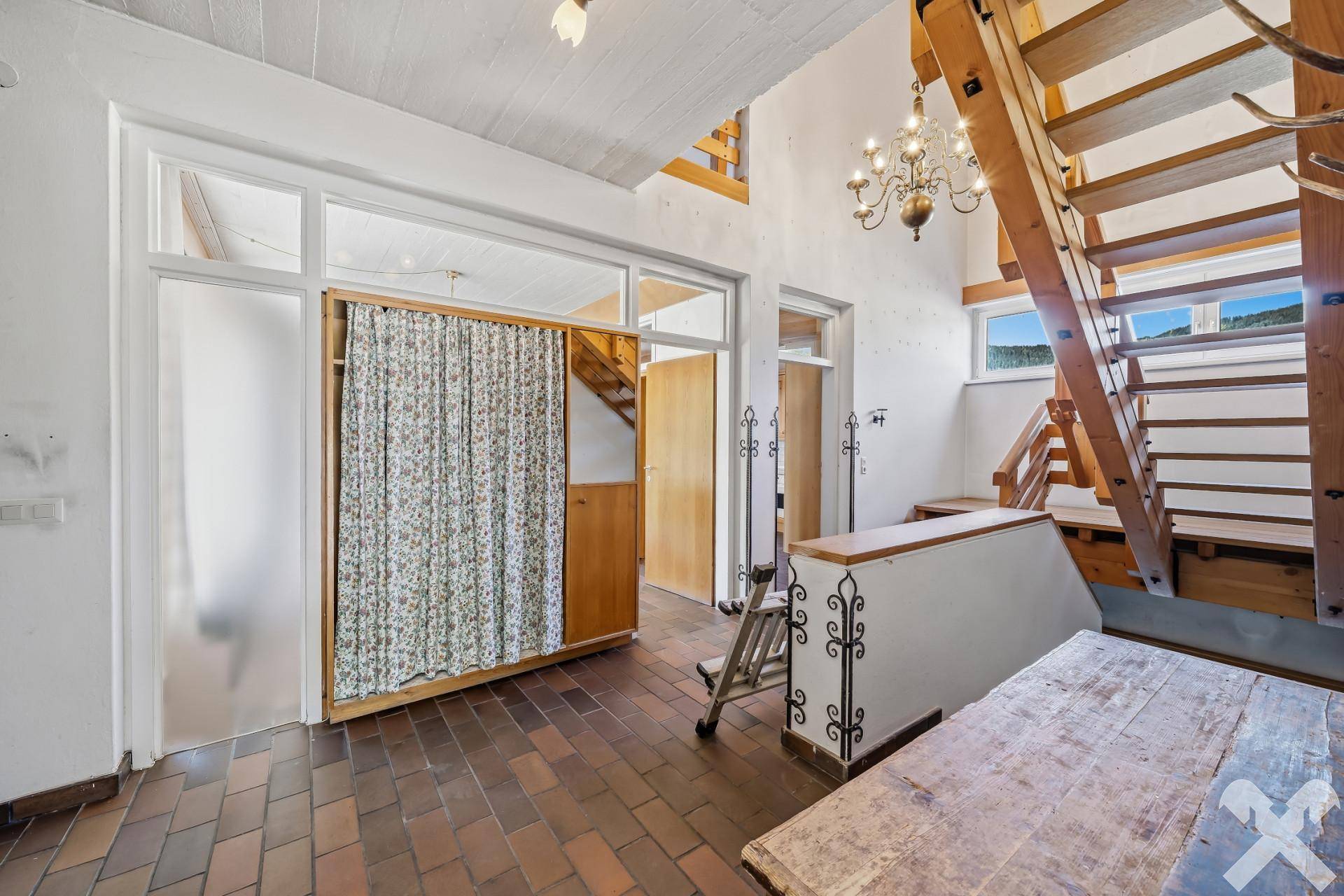 Eingangsbereich mit Fliesenboden, Holztreppe und Zugang zu weiteren Räumen.