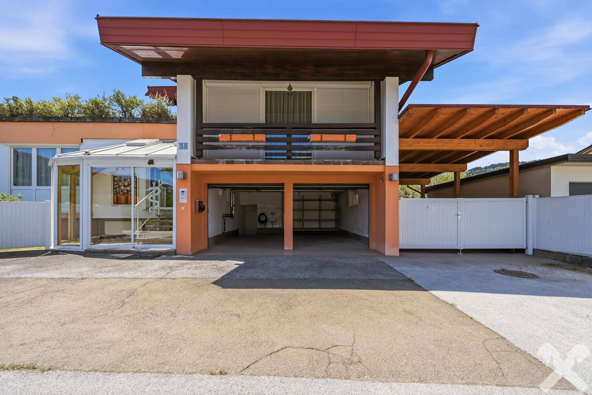 Vorderseite des Hauses mit offener Doppelgarage, Balkon und moderner Architektur.