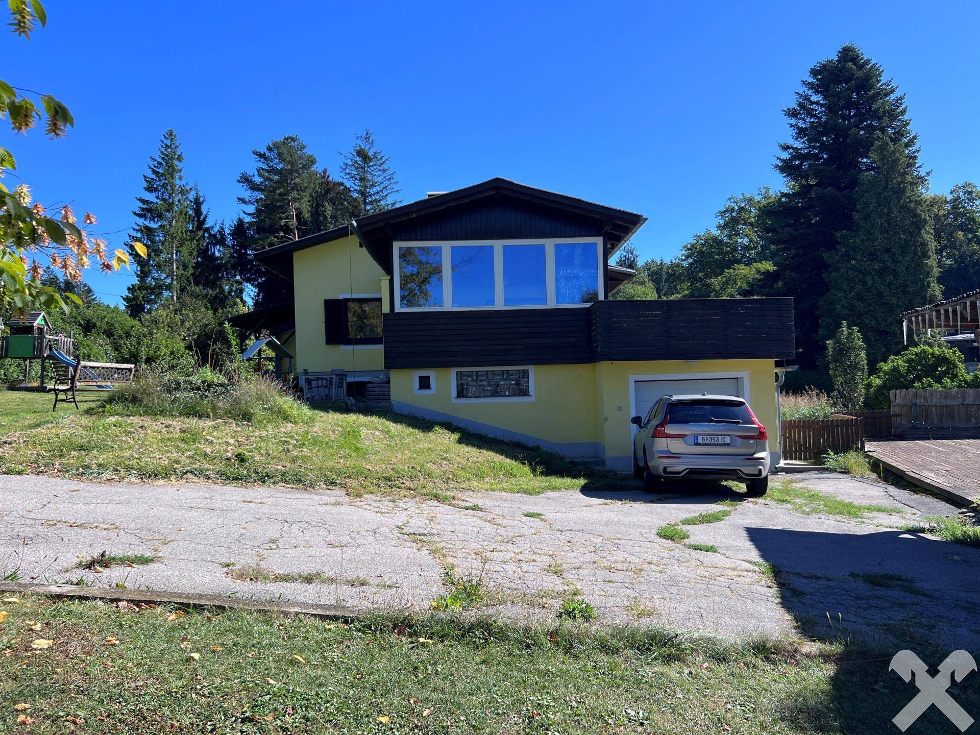 Vorderansicht des gelben Hauses mit Einfahrt, Garage und einem geparkten Auto davor.