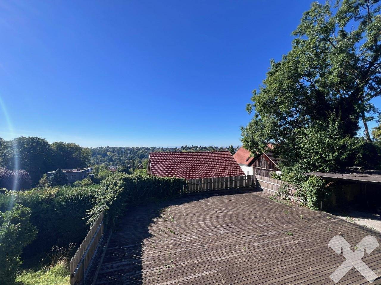 Geräumige Holzterrasse mit weitem Blick über die grüne Umgebung und die Dächer der Nachbarschaft.