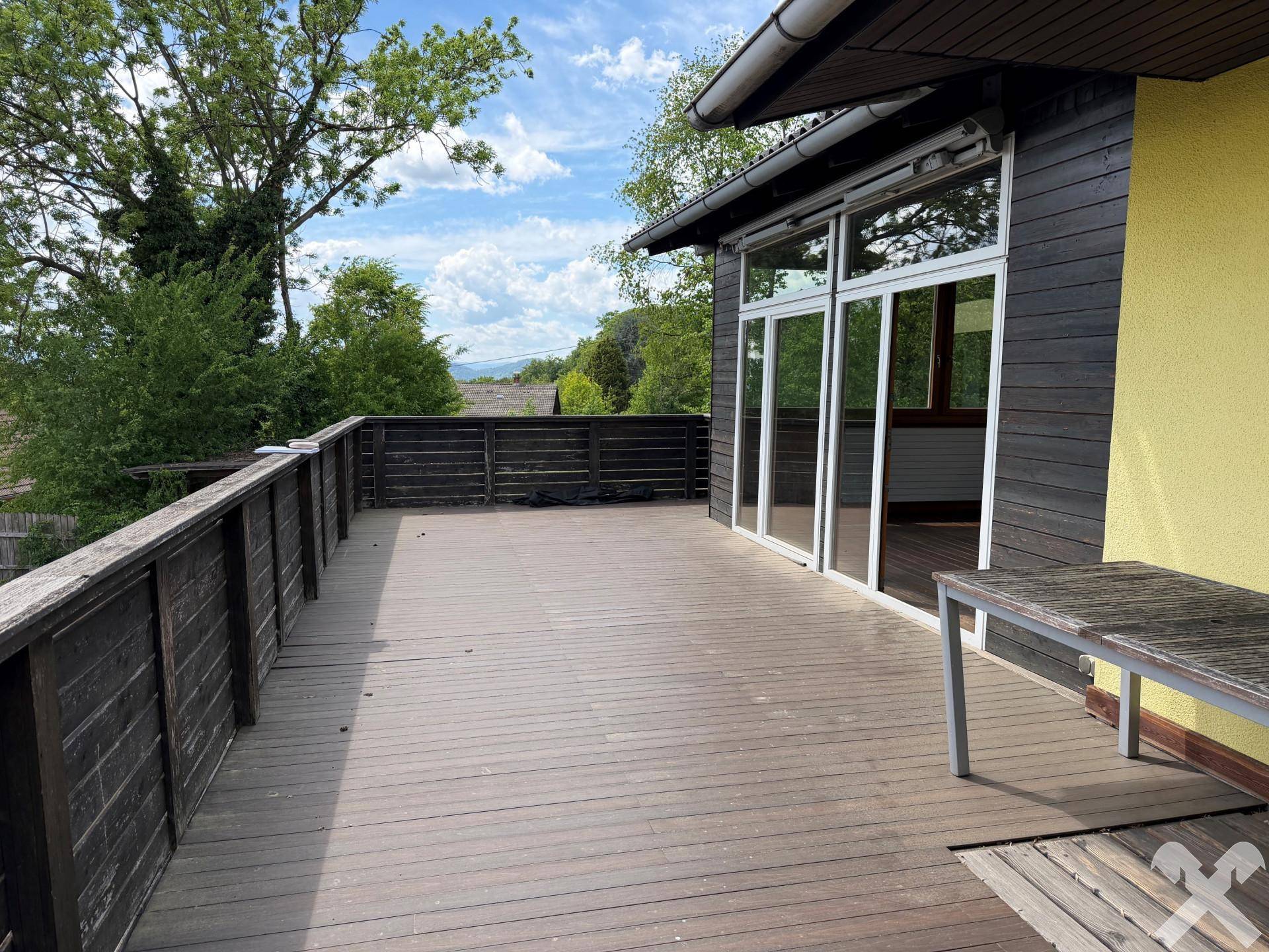 Geräumige Holzterrasse mit großen Glasfronten, die den Zugang zum Innenbereich ermöglichen.