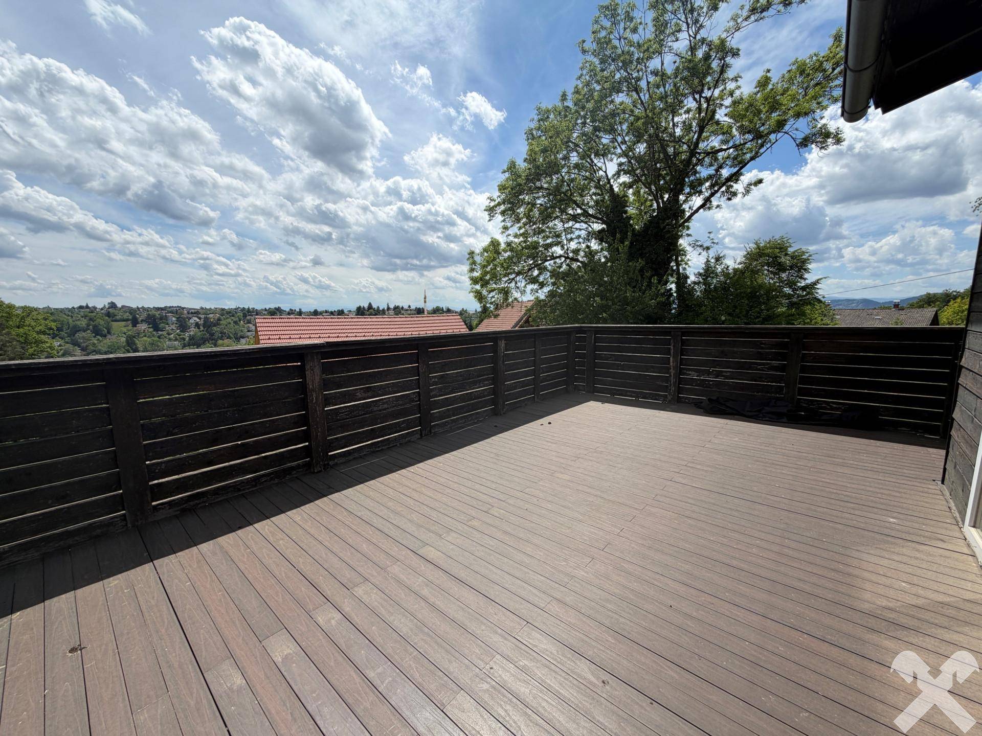 Große Holzterrasse mit dunklem Geländer und weitem Blick über die umliegende Landschaft.