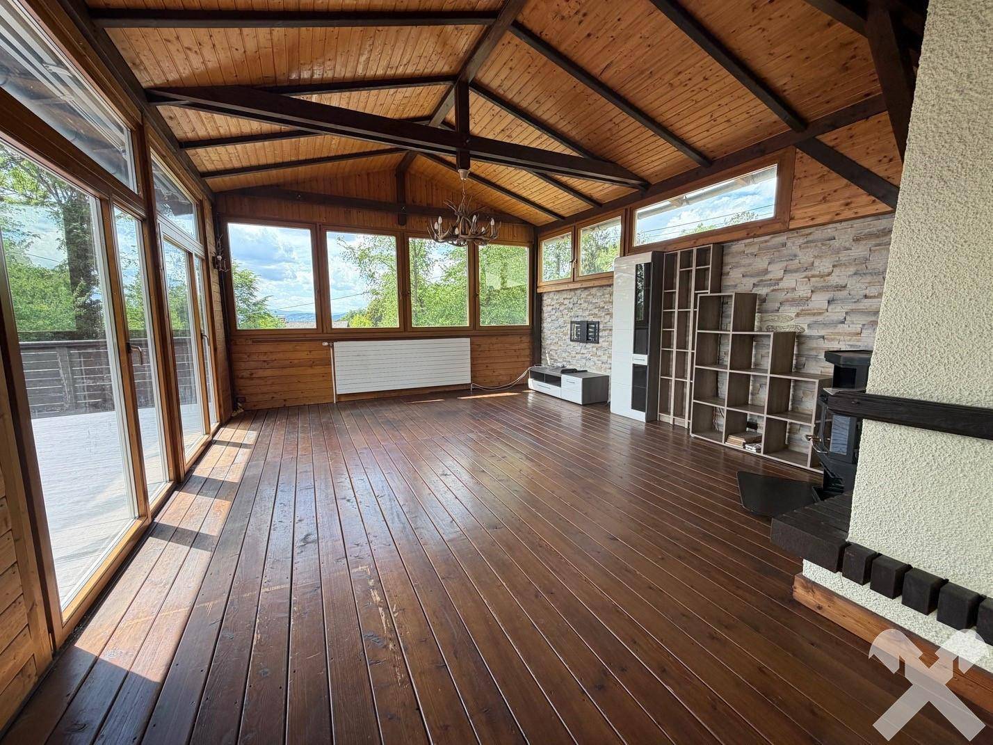 Gemütliches Wohnzimmer mit Holzböden, Holzdecken und einer Steinwand mit Kamin und großen Fenstern.