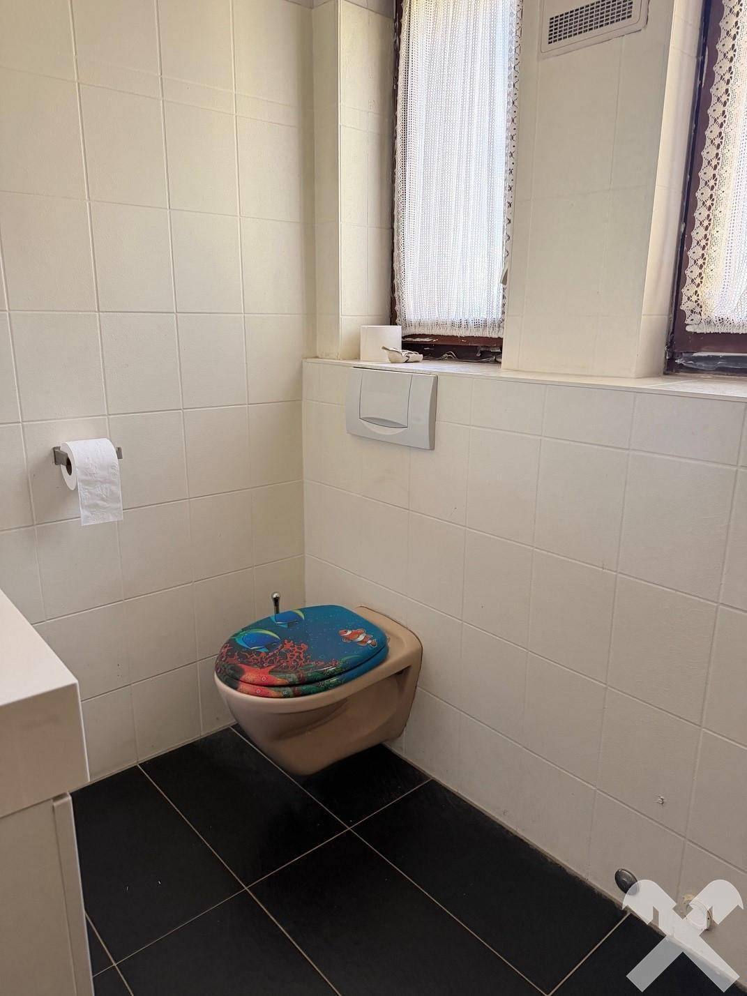 Toilettenbereich mit weißen Wandfliesen, einem Fenster und einer modernen Wandtoilette.