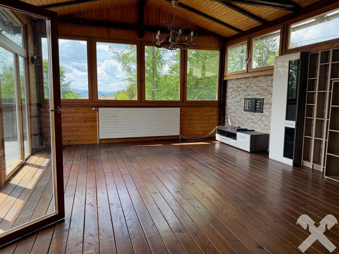 Helles Wohnzimmer mit Holzböden, Holzdecken und großen Fenstern, die viel Tageslicht hereinlassen.