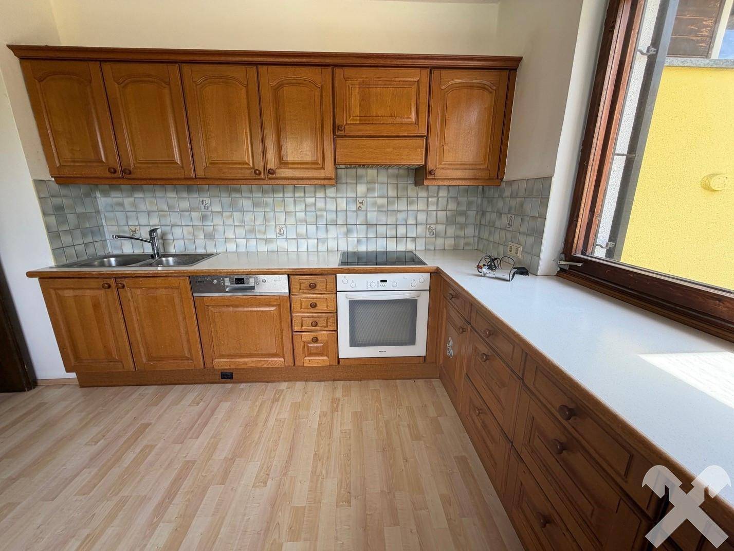 Funktionale Küche mit Holzschränken, hellen Arbeitsplatten und integrierten Elektrogeräten.