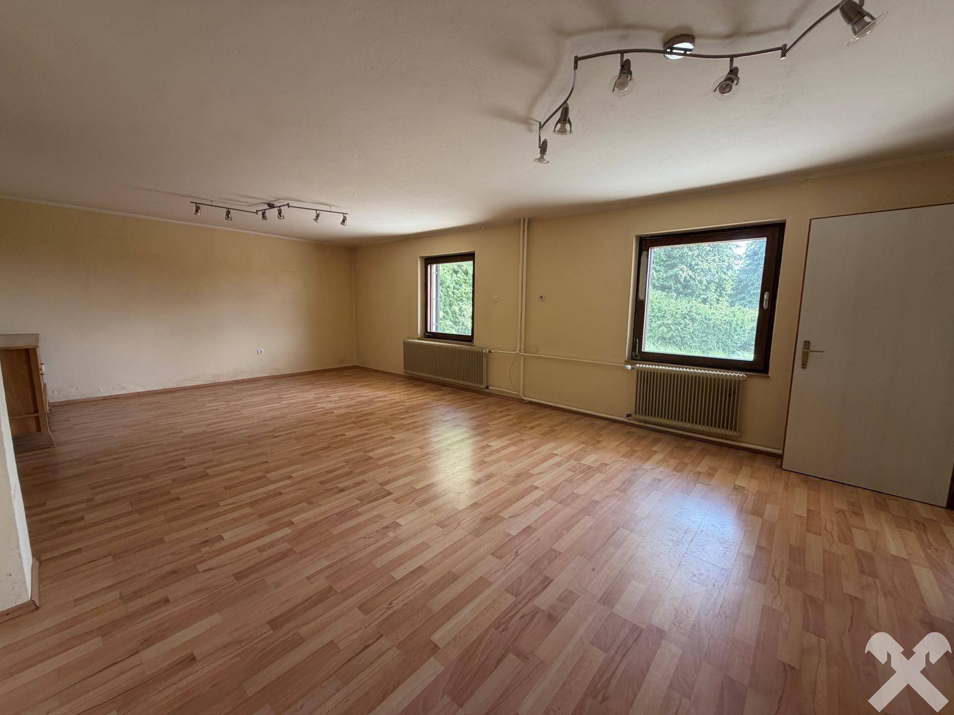Helles Wohnzimmer mit Laminatboden und Blick ins Grüne durch die Fenster.