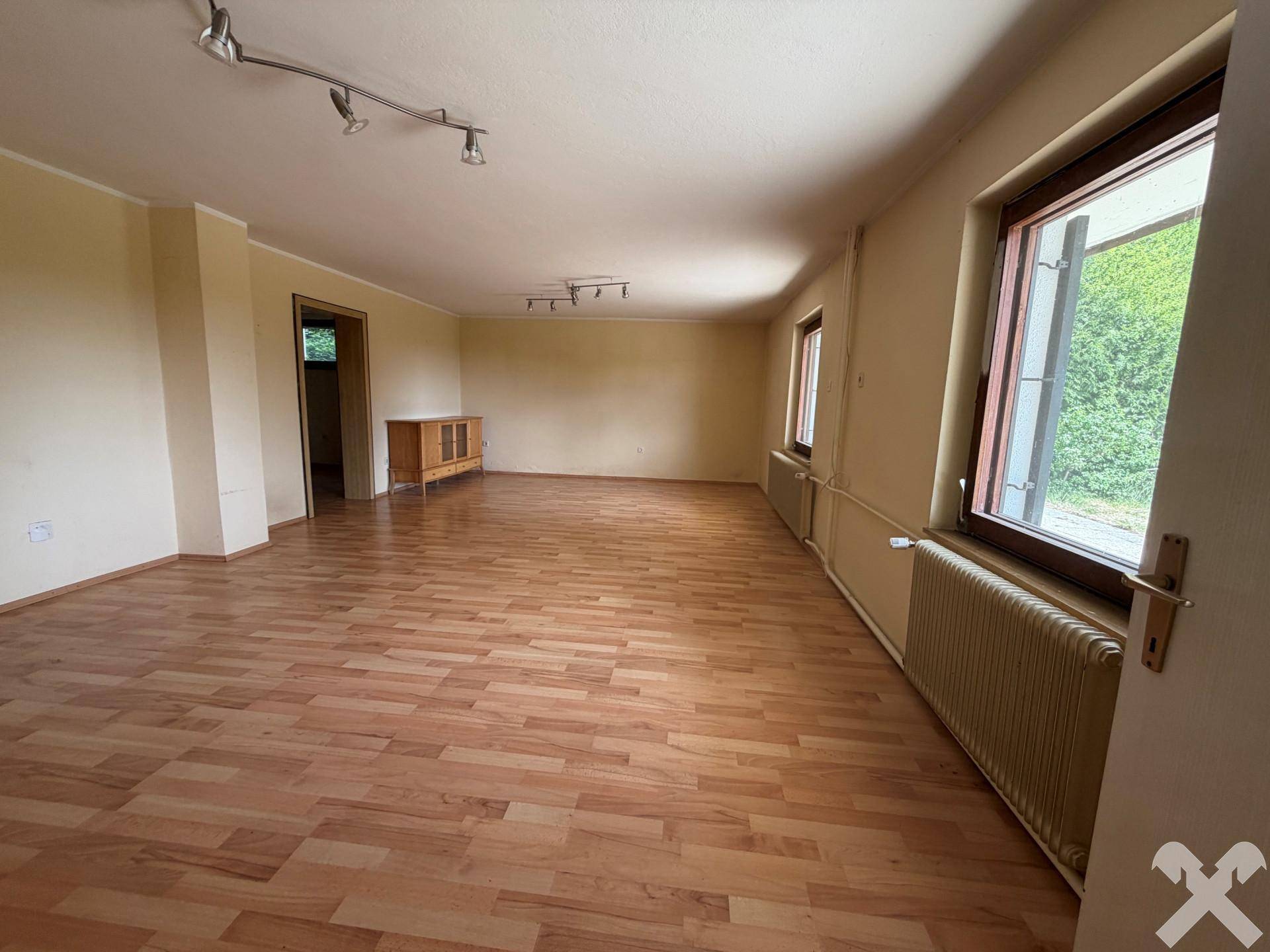 Geräumiges Wohnzimmer mit Laminatboden und mehreren Fenstern, bereit zur individuellen Gestaltung.