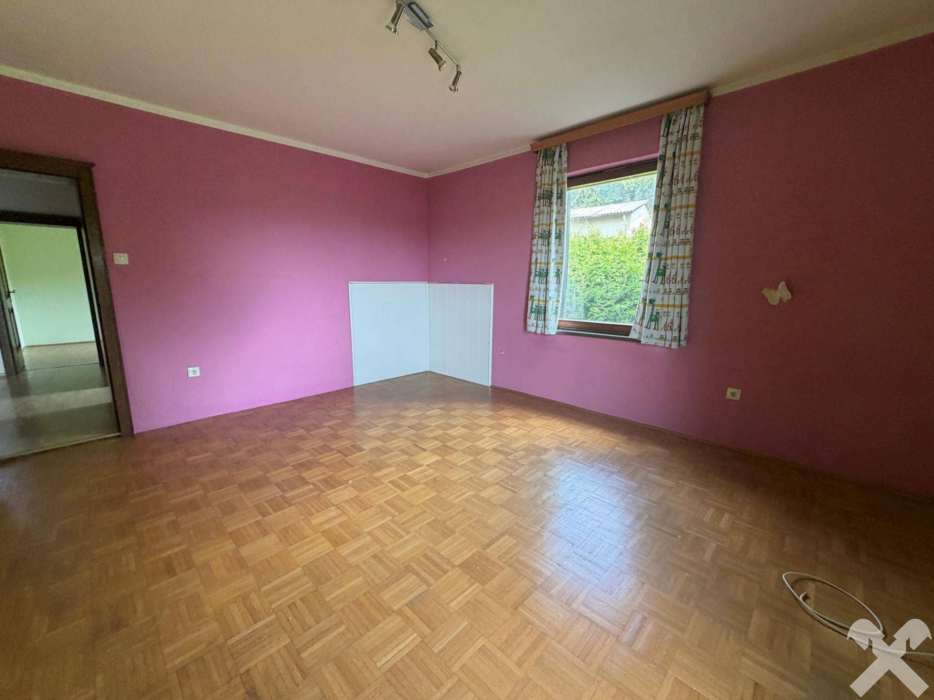 Geräumiges Zimmer mit rosa Wänden, Parkettboden und einem Fenster, das viel Licht hereinlässt.
