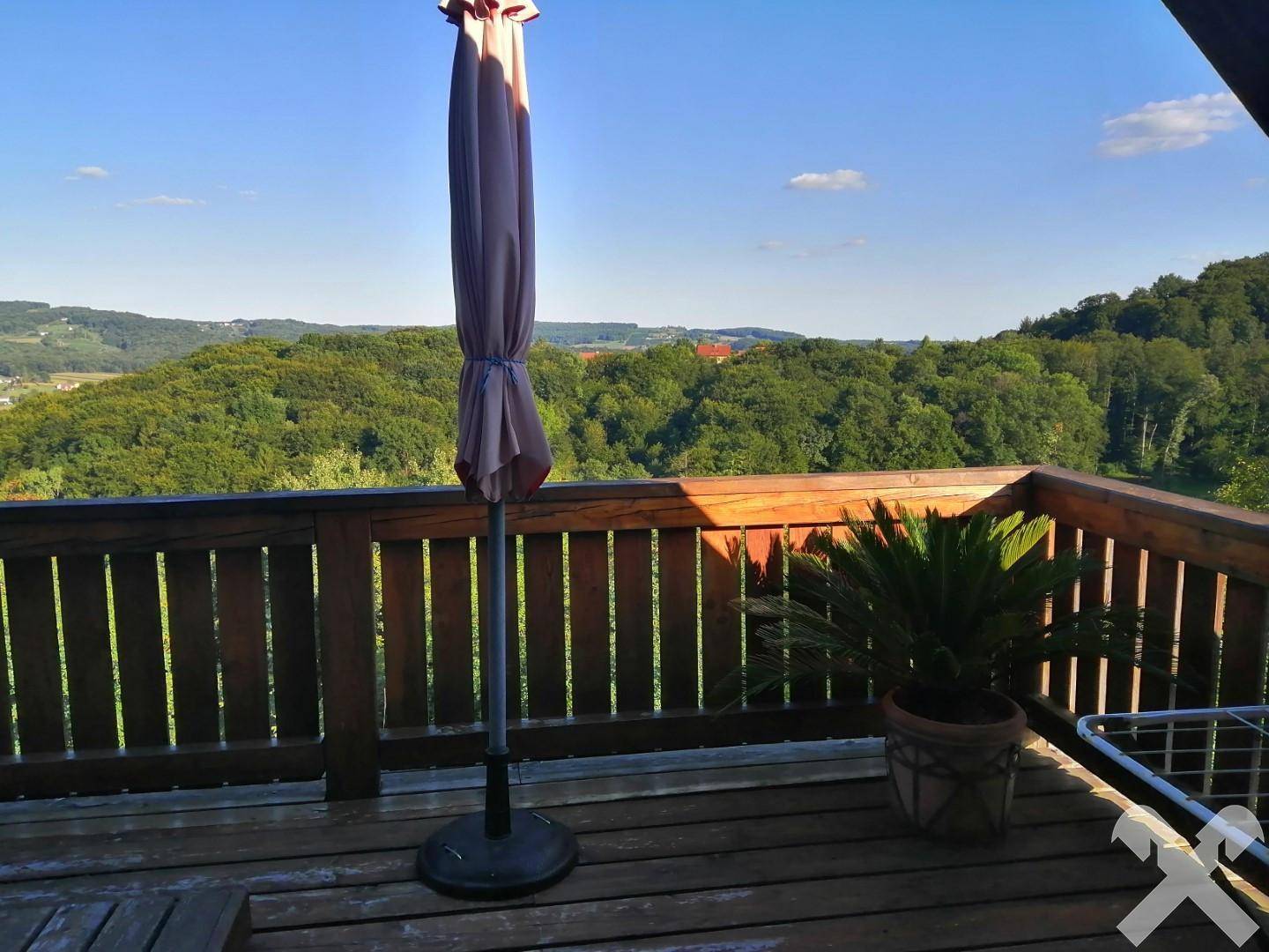 Geräumiger Holzbalkon mit weitem Blick über eine grüne Hügellandschaft und Wälder.