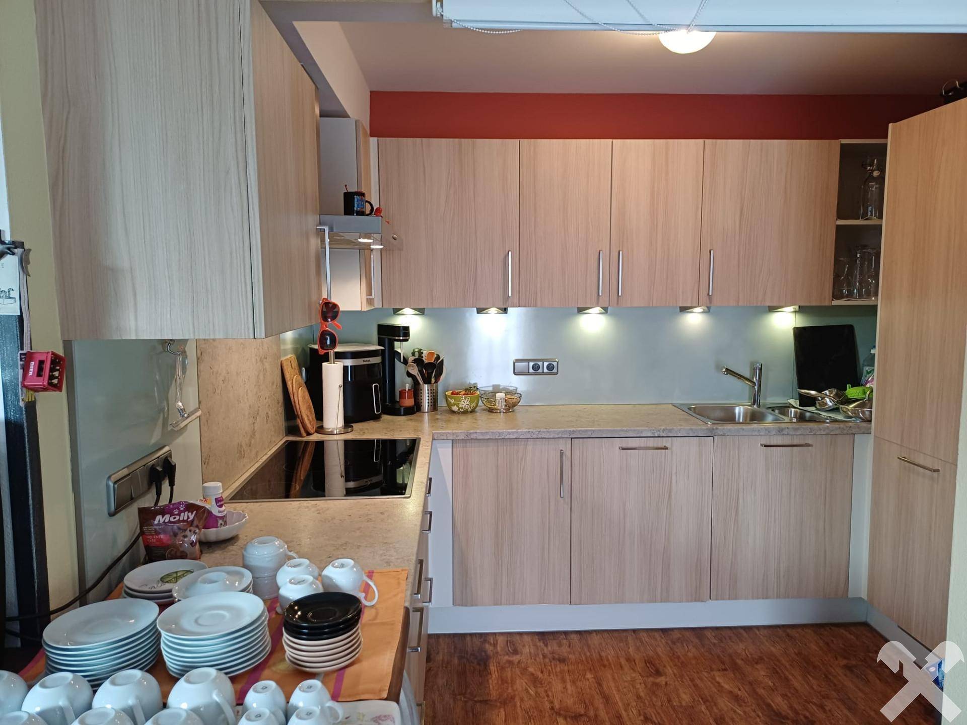 Moderne Küche mit hellen Holzschränken, Edelstahlrückwand und integrierten Geräten.