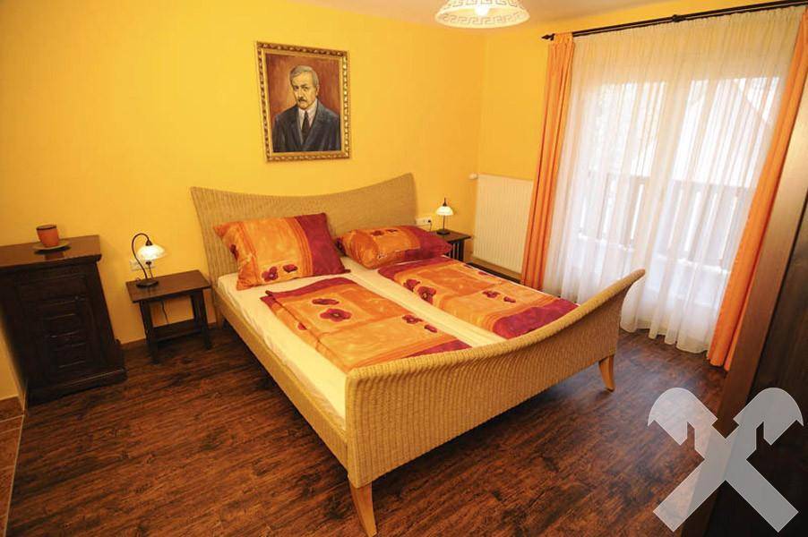 Freundliches Schlafzimmer mit Doppelbett im Korbflecht-Stil, Holzboden und gelben Wänden.