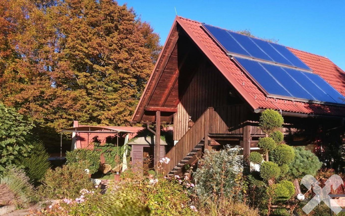 Charmantes Holzhaus mit Solaranlage auf dem Dach, umgeben von herbstlicher Vegetation und Bäumen.