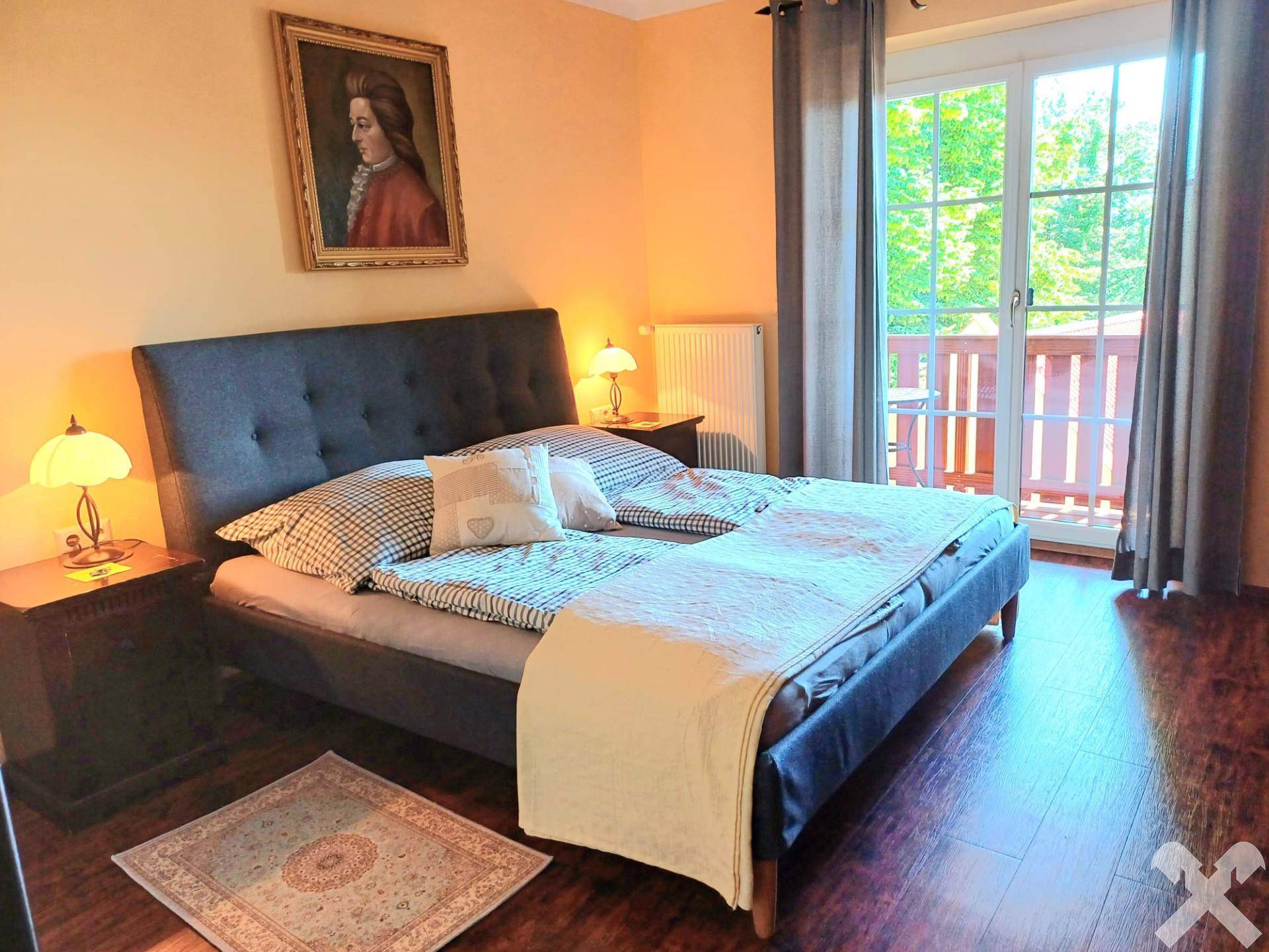 Helles Schlafzimmer mit Doppelbett, Holzboden und direktem Zugang zu einem Balkon.