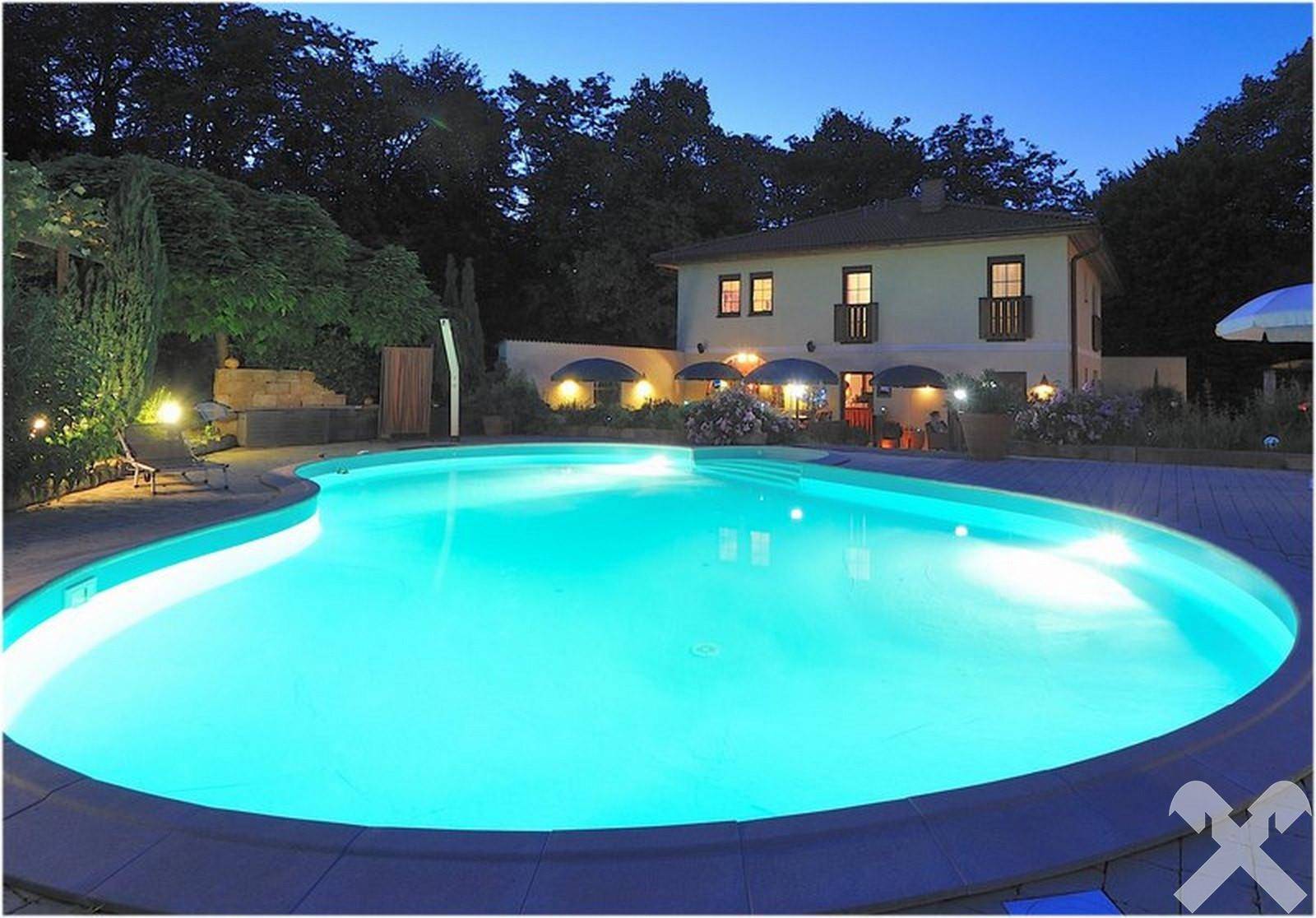 Beleuchteter Poolbereich bei Nacht mit dem Haupthaus im Hintergrund, eine stimmungsvolle Atmosphäre.