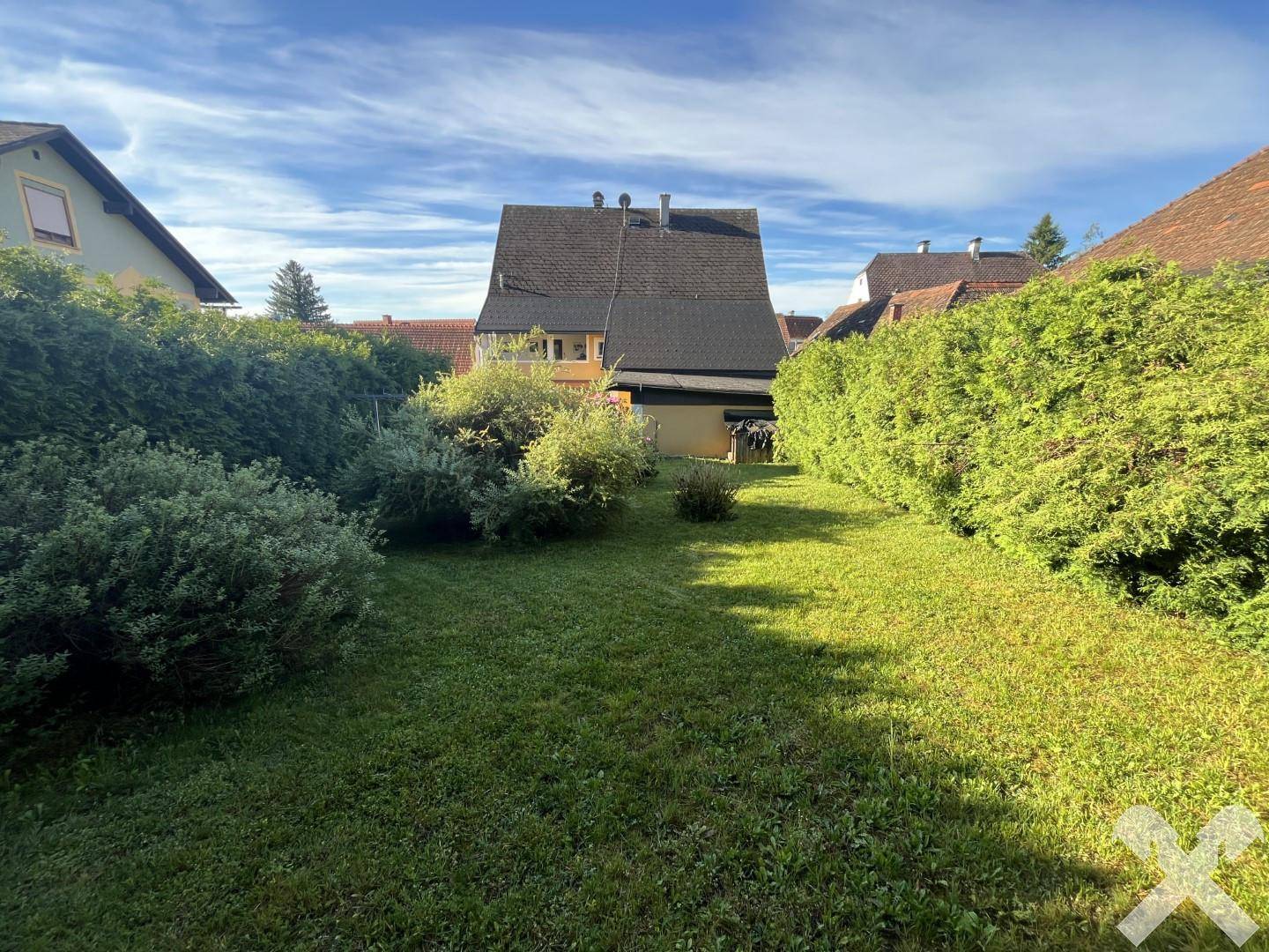 Sonniger Garten mit Rasenfläche, umgeben von hohen Hecken und Blick auf das Hauptgebäude.