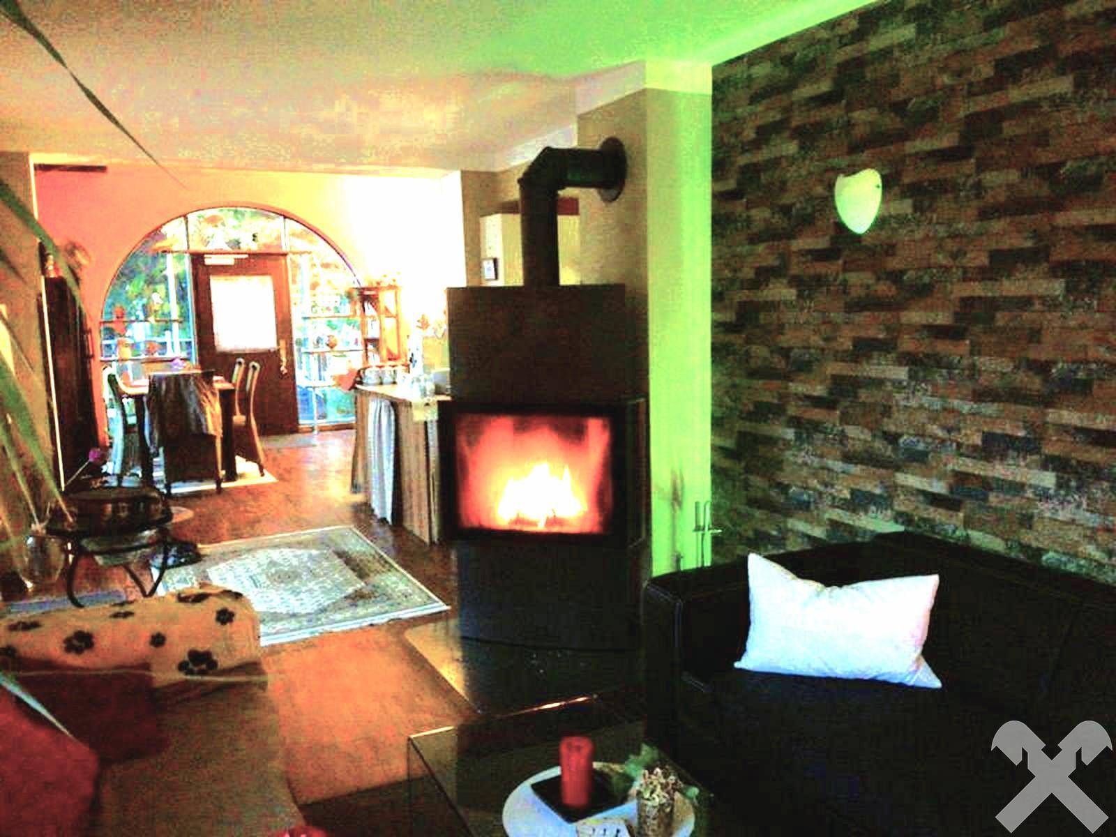 Gemütliches Wohnzimmer mit modernem Holzofen, Steinwand und bequemer Sitzecke.