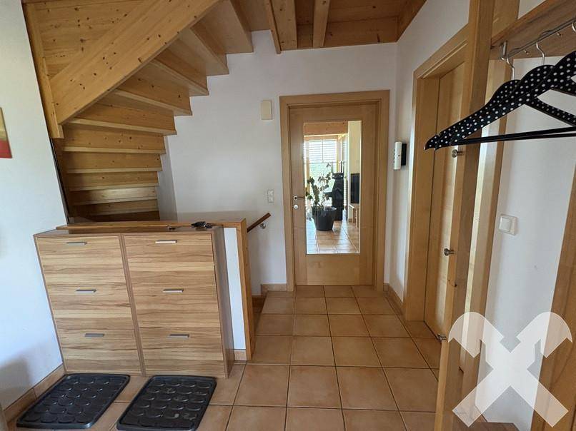 Heller Eingangsbereich mit Holztreppe, Fliesenboden und Garderobe, führt in den Wohnbereich.