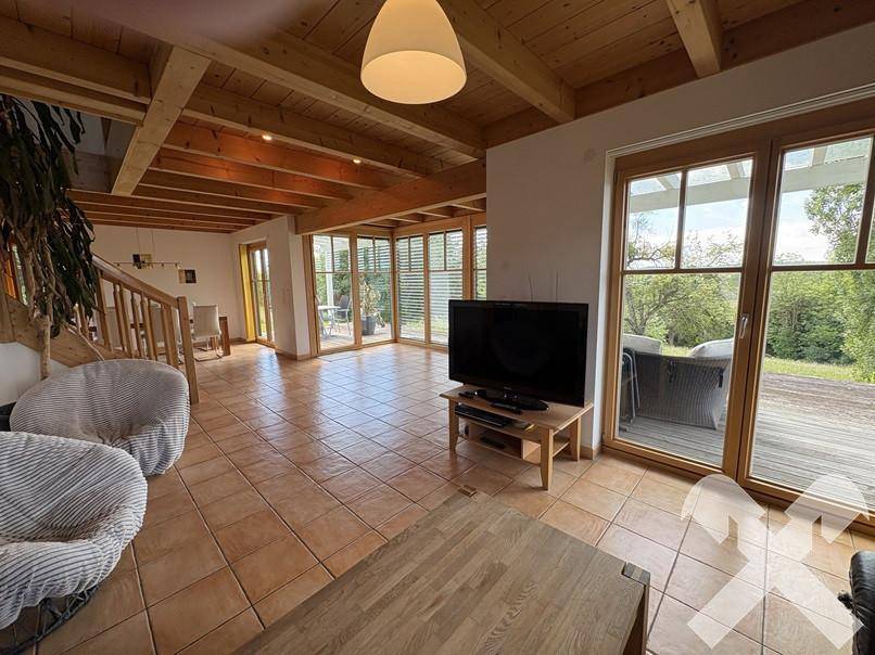 Geräumiges Wohnzimmer mit Fliesenboden, Holzbalkendecke und großen Fenstern mit Zugang zur Terrasse.