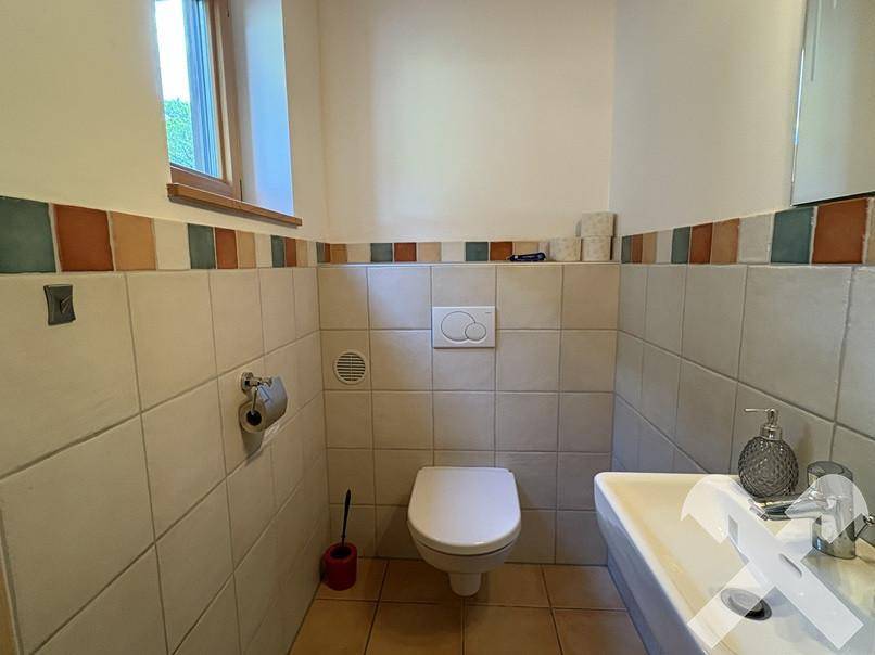 Kleines Gäste-WC mit Wand-WC, Waschbecken und farbigen Fliesen als Akzent.