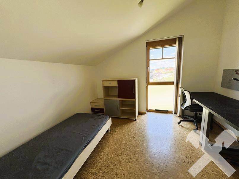 Helles Kinderzimmer mit Korkboden, Einzelbett und Schreibtisch, unter der Dachschräge.