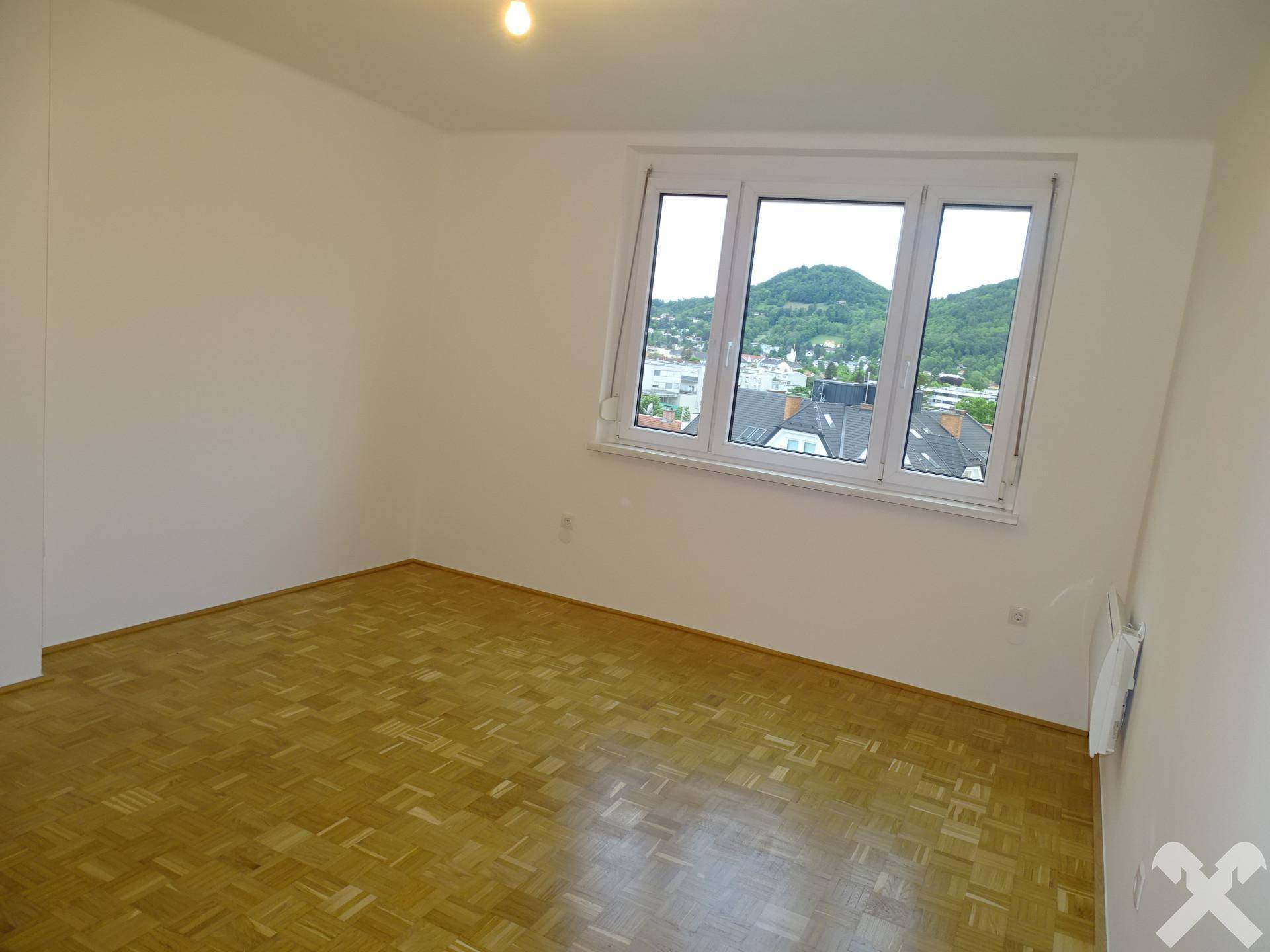 Helles Zimmer mit Parkettboden und Fensterblick auf die umliegende Landschaft.