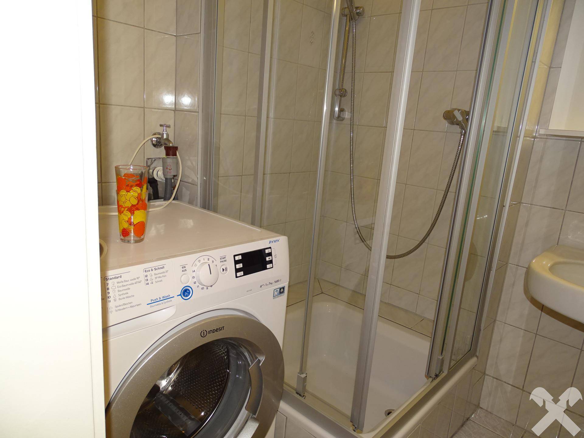 Badezimmer mit Duschkabine und integrierter Waschmaschine, praktisch und platzsparend.