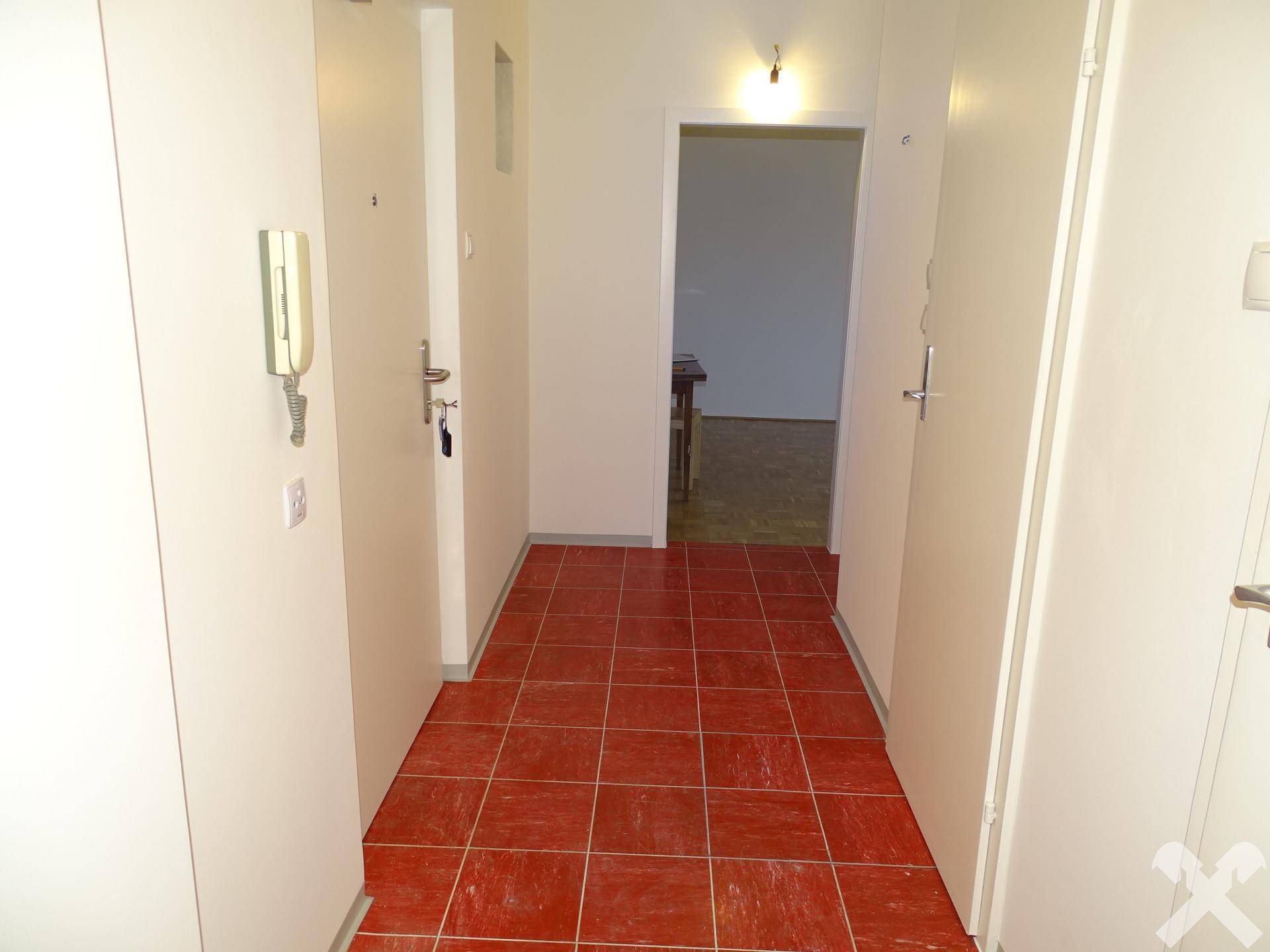 Flur mit roten Fliesen und Gegensprechanlage, verbindet verschiedene Räume.